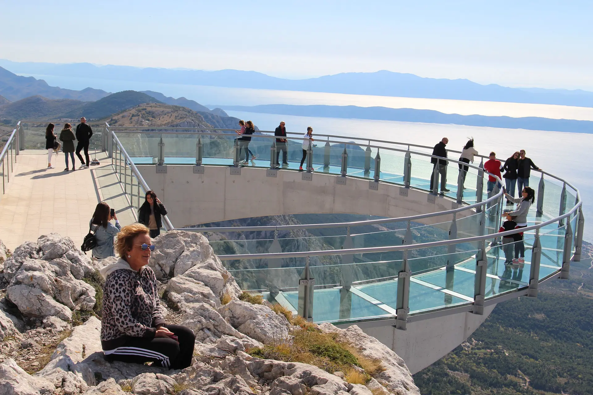Besucher auf dem gläsernen Hufeisen des Biokovo-Skywalks, tief unten die Küste von Makarska