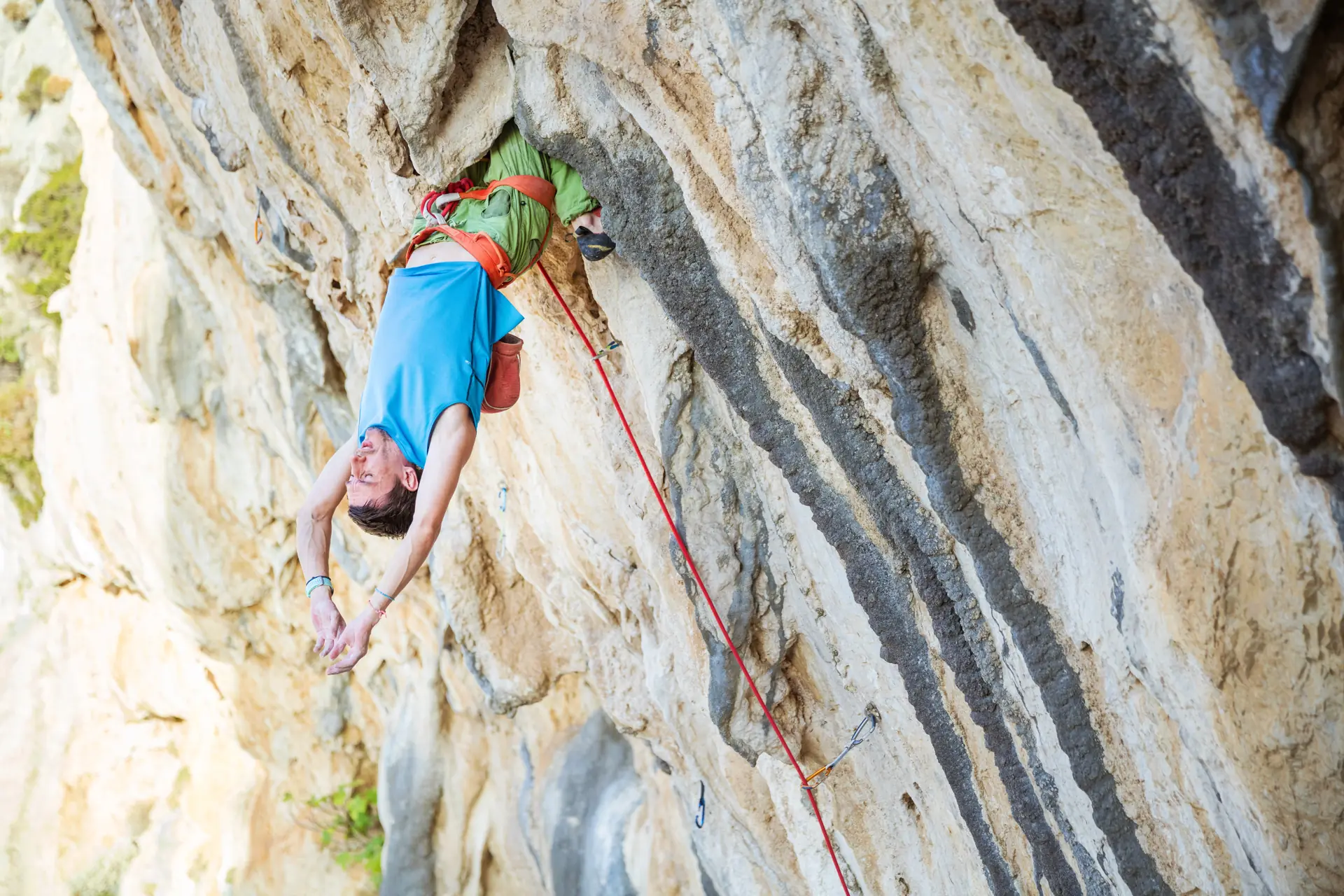 A climber in a blue shirt resting upside down on a rope against a grey limestone wall (symbolic image, not Reimers Ranch)