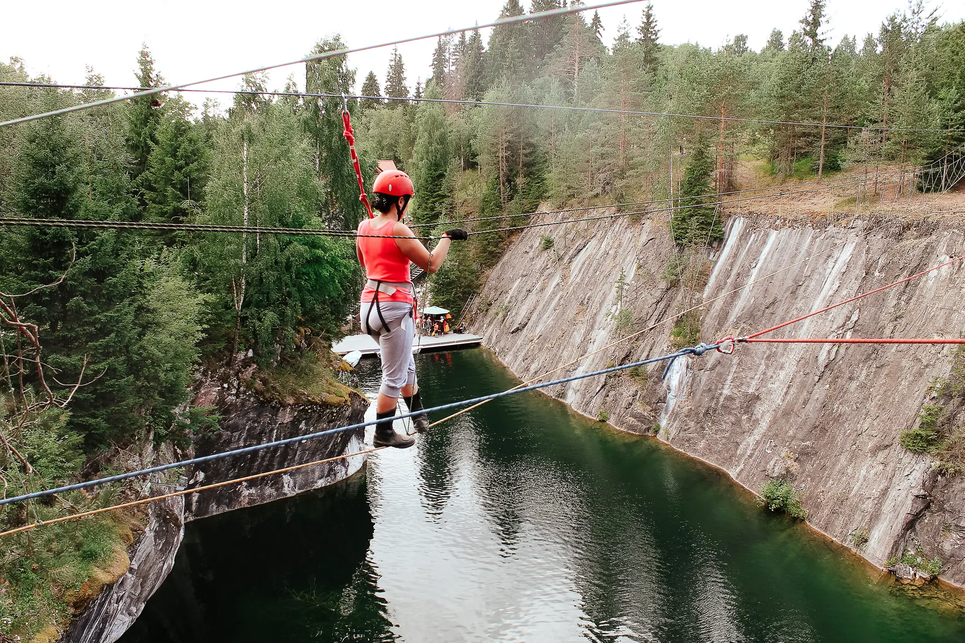 A rider in helmet and harness on a zipline crossing a green quarry lake between cliffs (symbolic image, not Lake Travis)