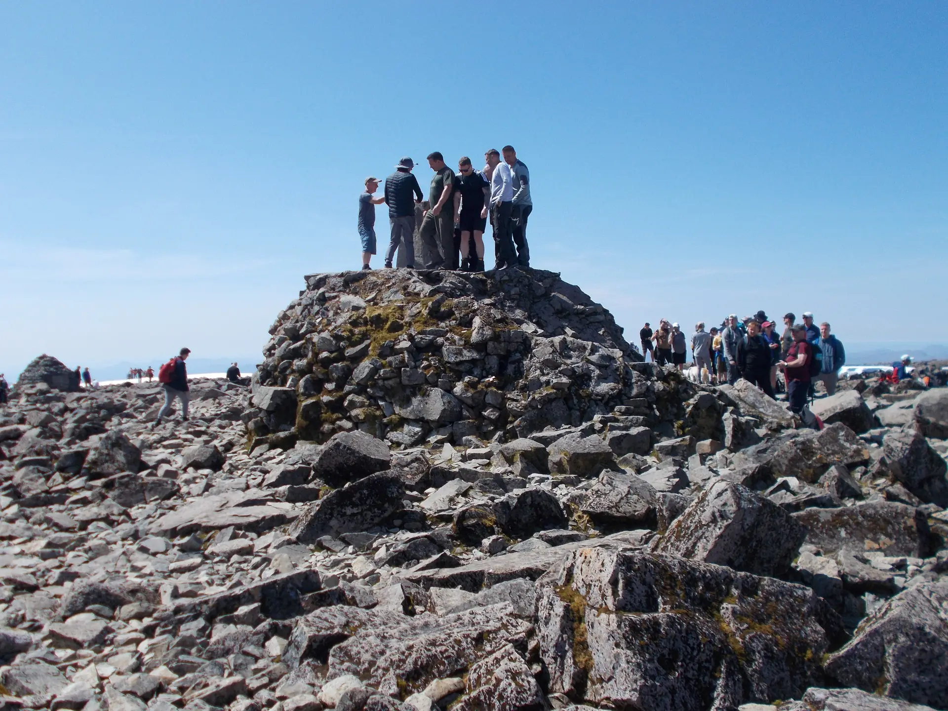 Wanderer am Gipfelsteinmann des Ben Nevis unter blauem Himmel