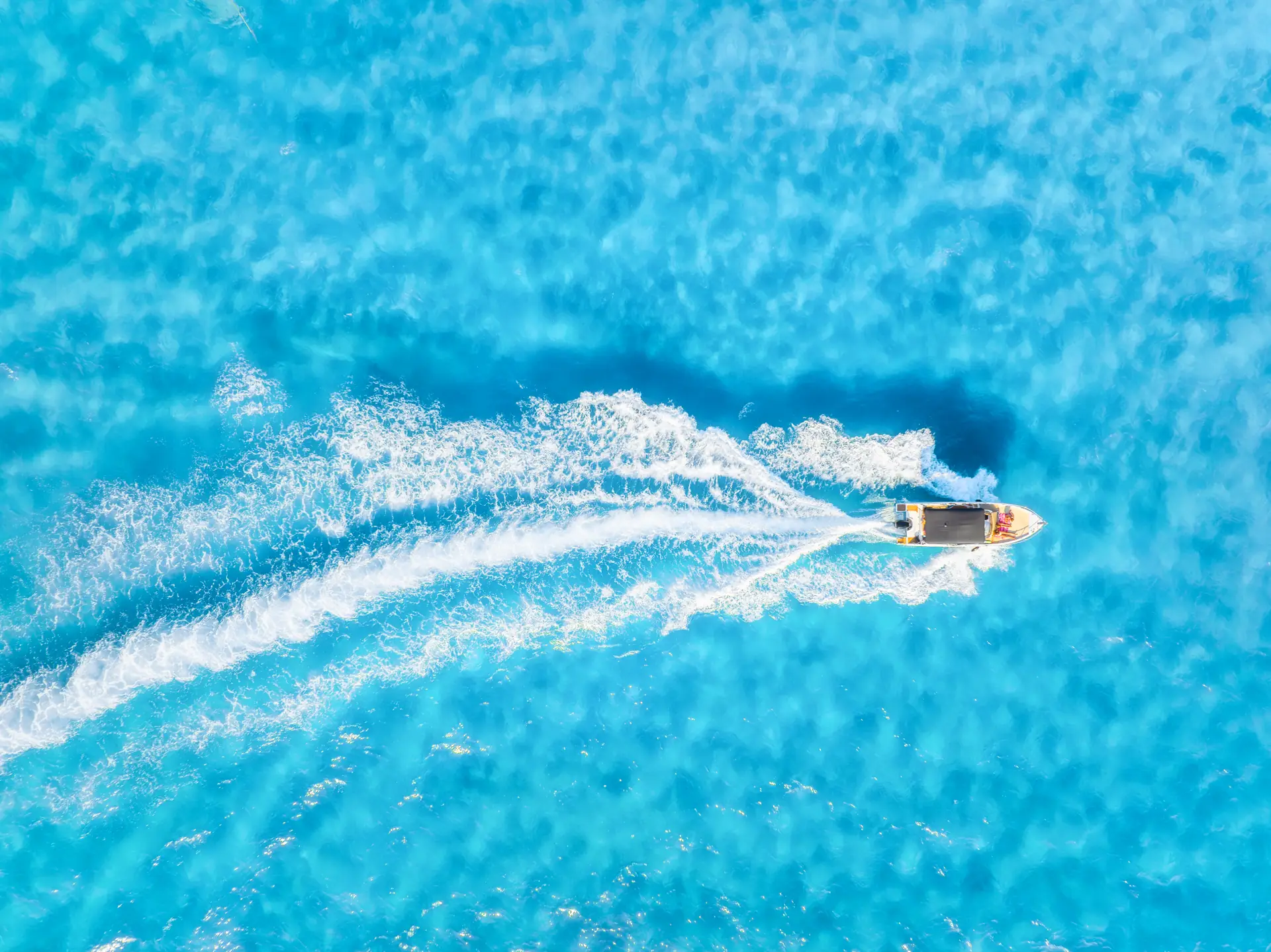 A small speedboat cutting a white wake across turquoise water, seen from above (symbolic image, Mallorca, not the Nichupté lagoon)