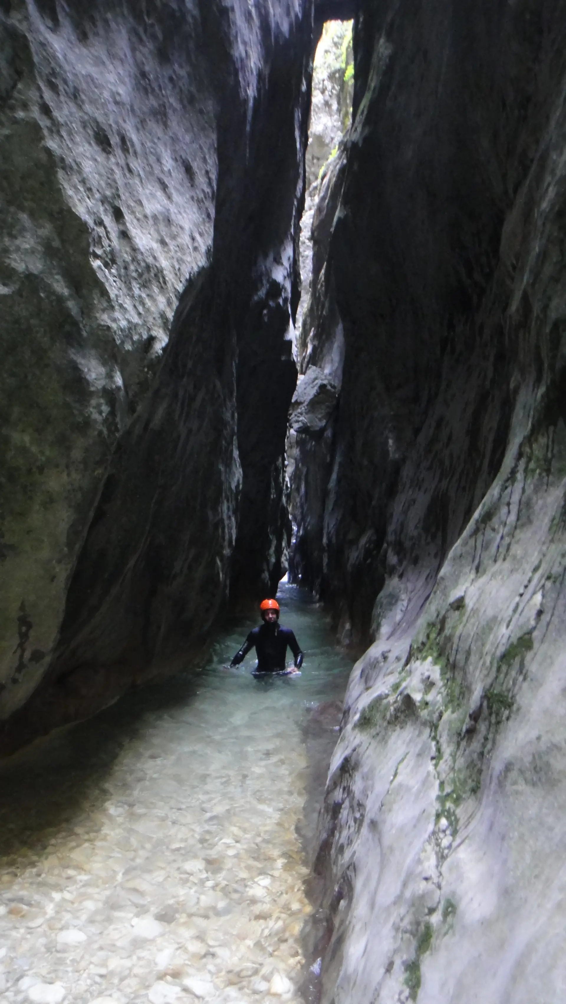 A canyoner in a helmet wading through the dark, narrow slot of the Nevidio canyon