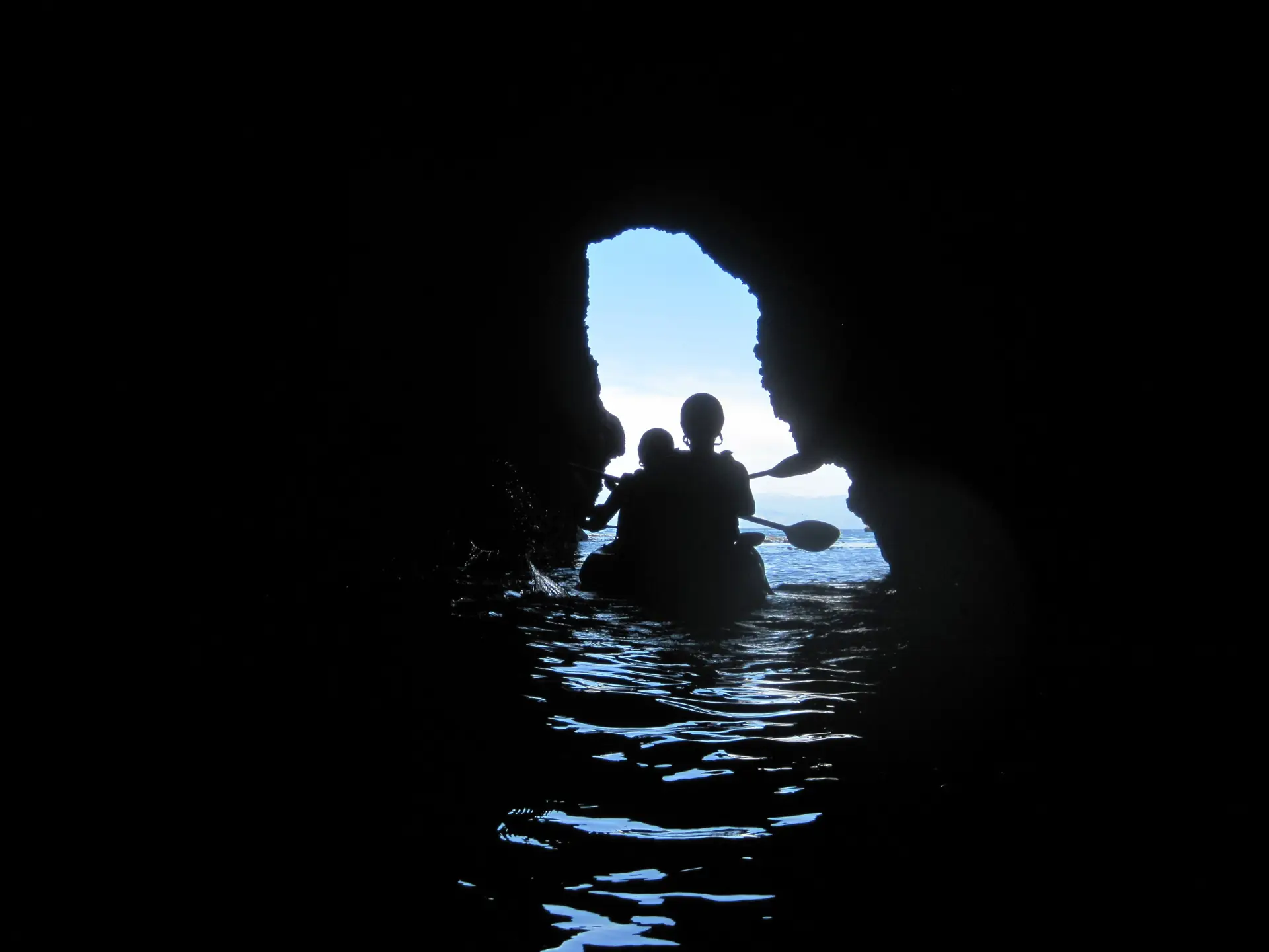 Kayakers inside a sea cave, light from the entrance on the water