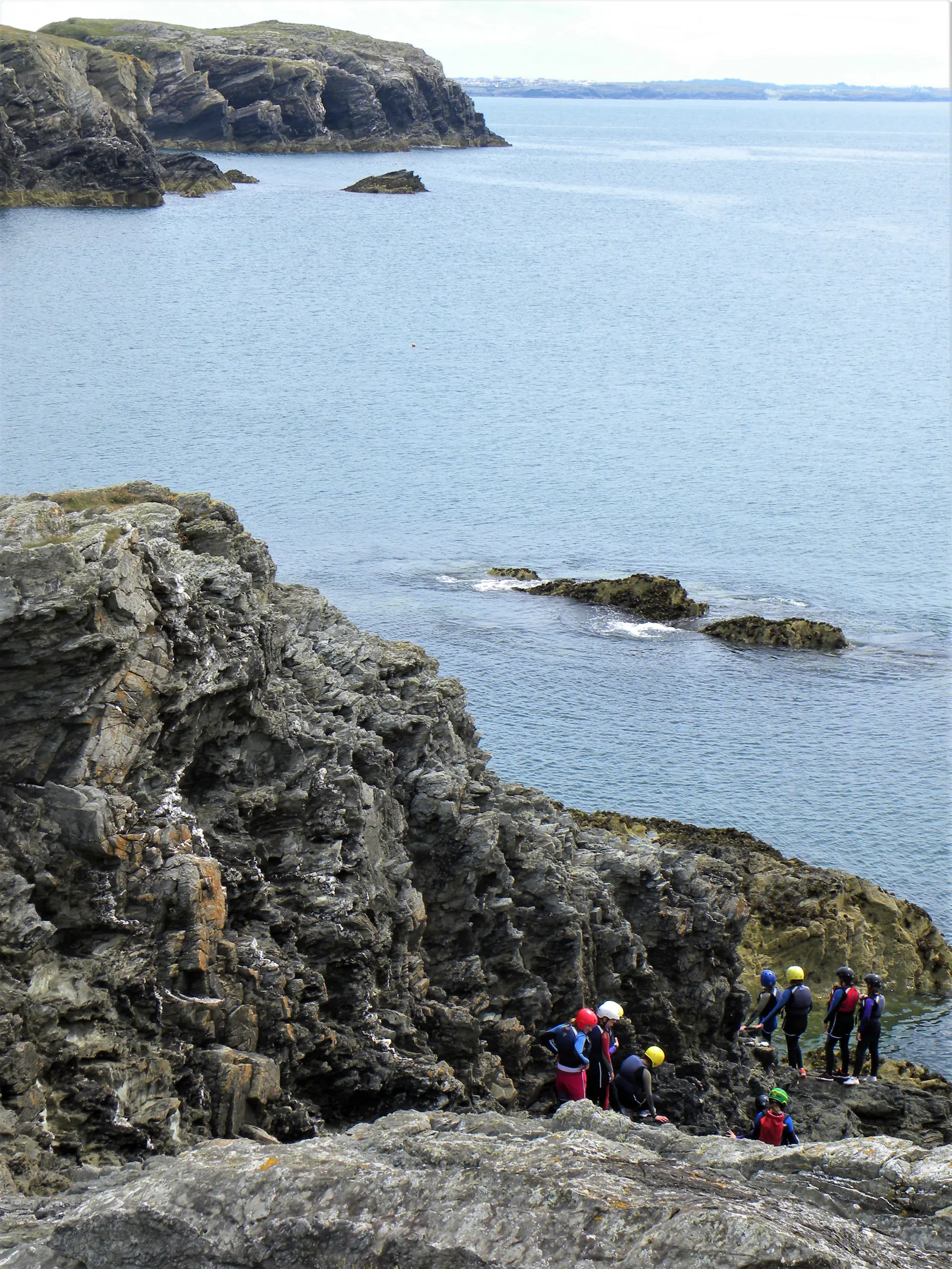 Eine Coasteering-Gruppe in Neopren an den Klippen bei Porth Ruffydd