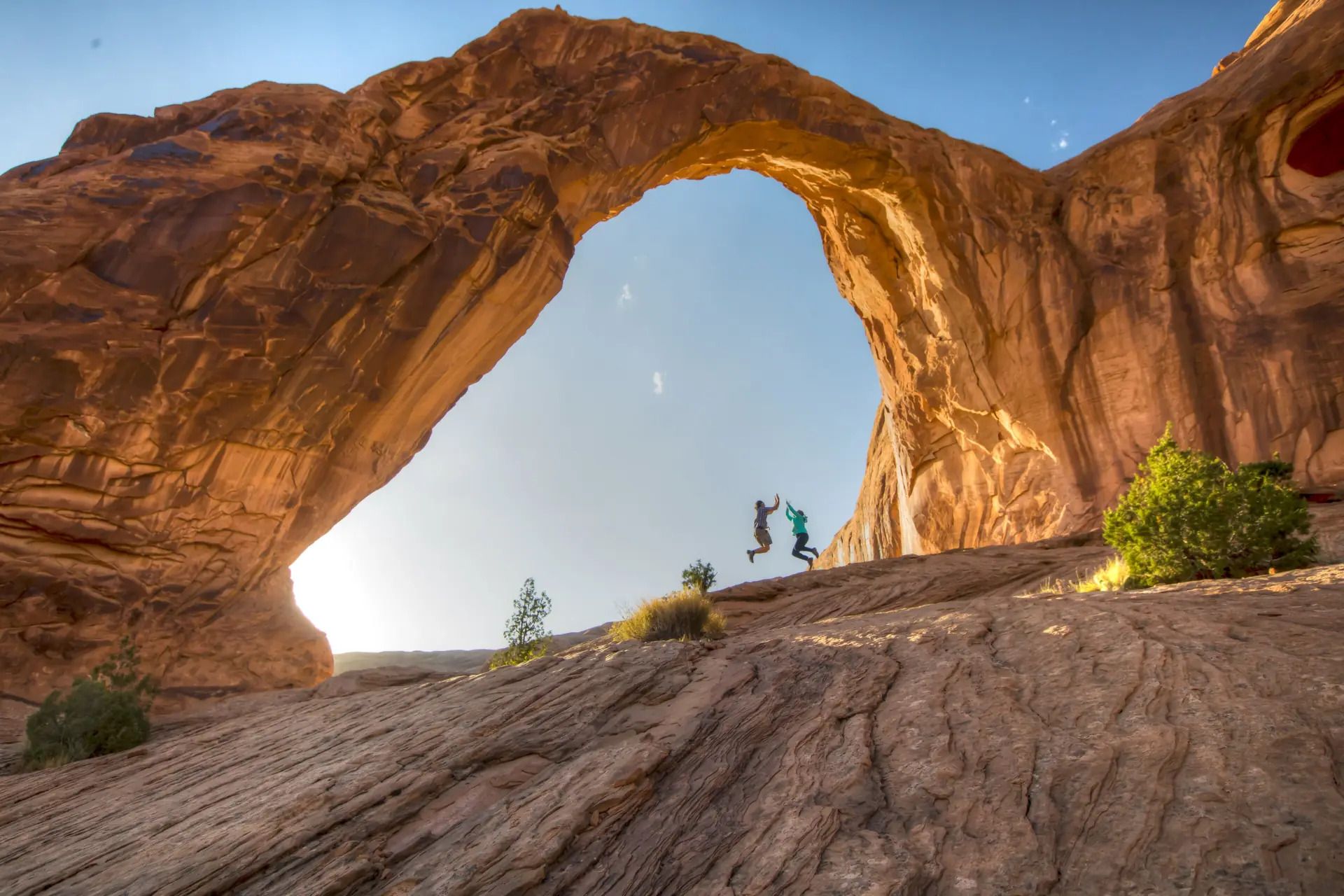Two people jumping on the slickrock beneath Corona Arch west of Moab