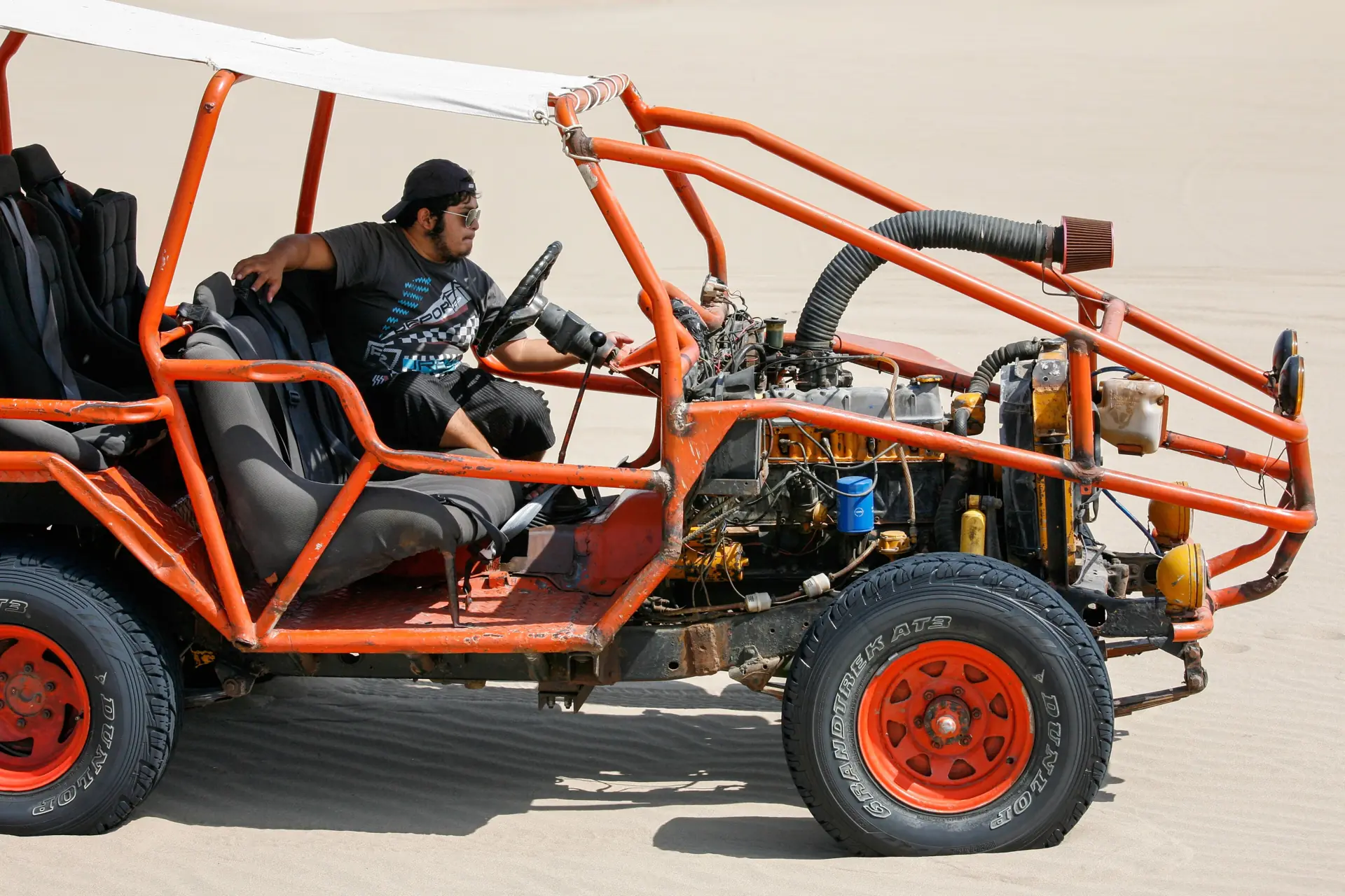 Ein Fahrer am Steuer eines offenen Dünenbuggys auf dem Sand von Huacachina, Überrollkäfig und Stollenreifen in der Sonne