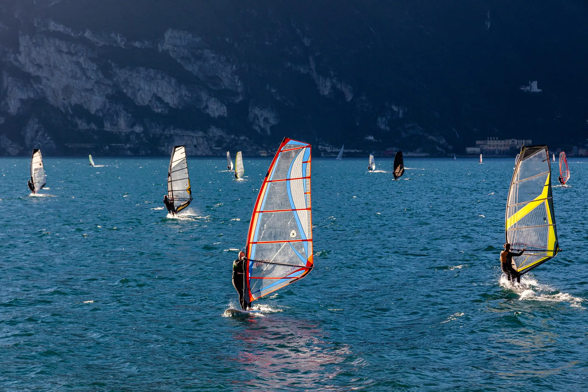 Windsurfer mit bunten Segeln vor Torbole am Nordende des Gardasees