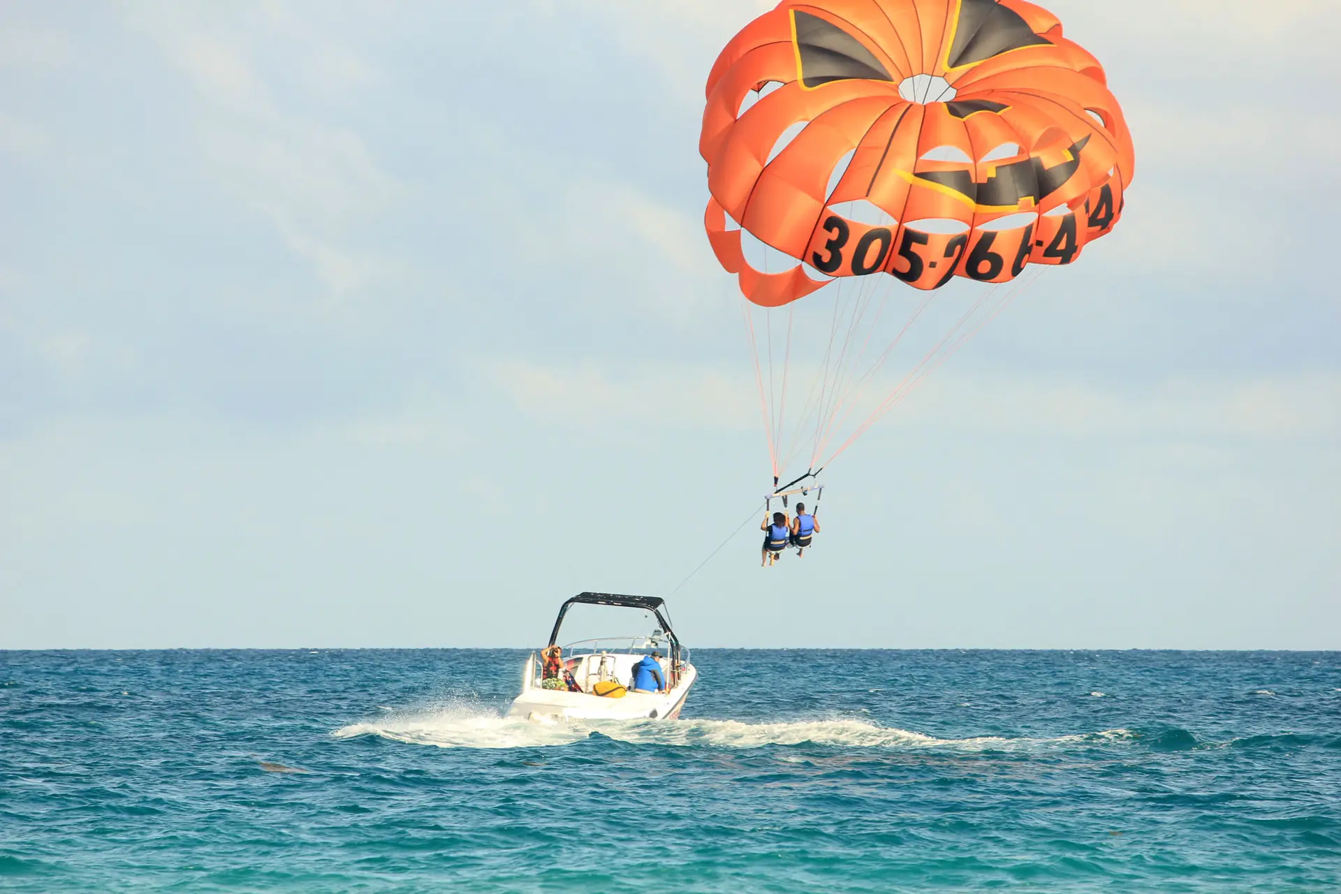 Two people under an orange parasail canopy towed by a boat off Miami