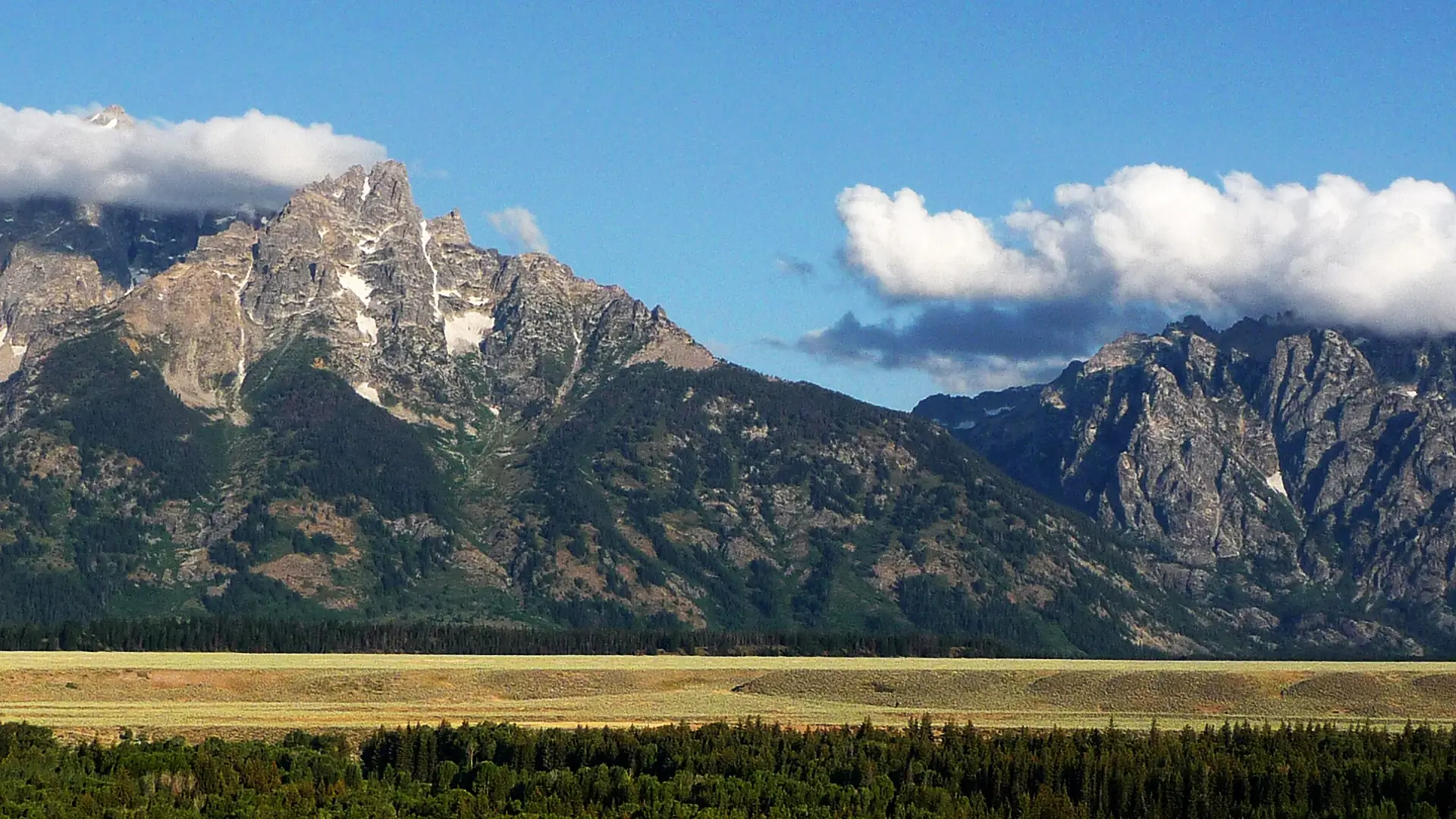 The Teton Range rising above the flats of Jackson Hole under summer cloud