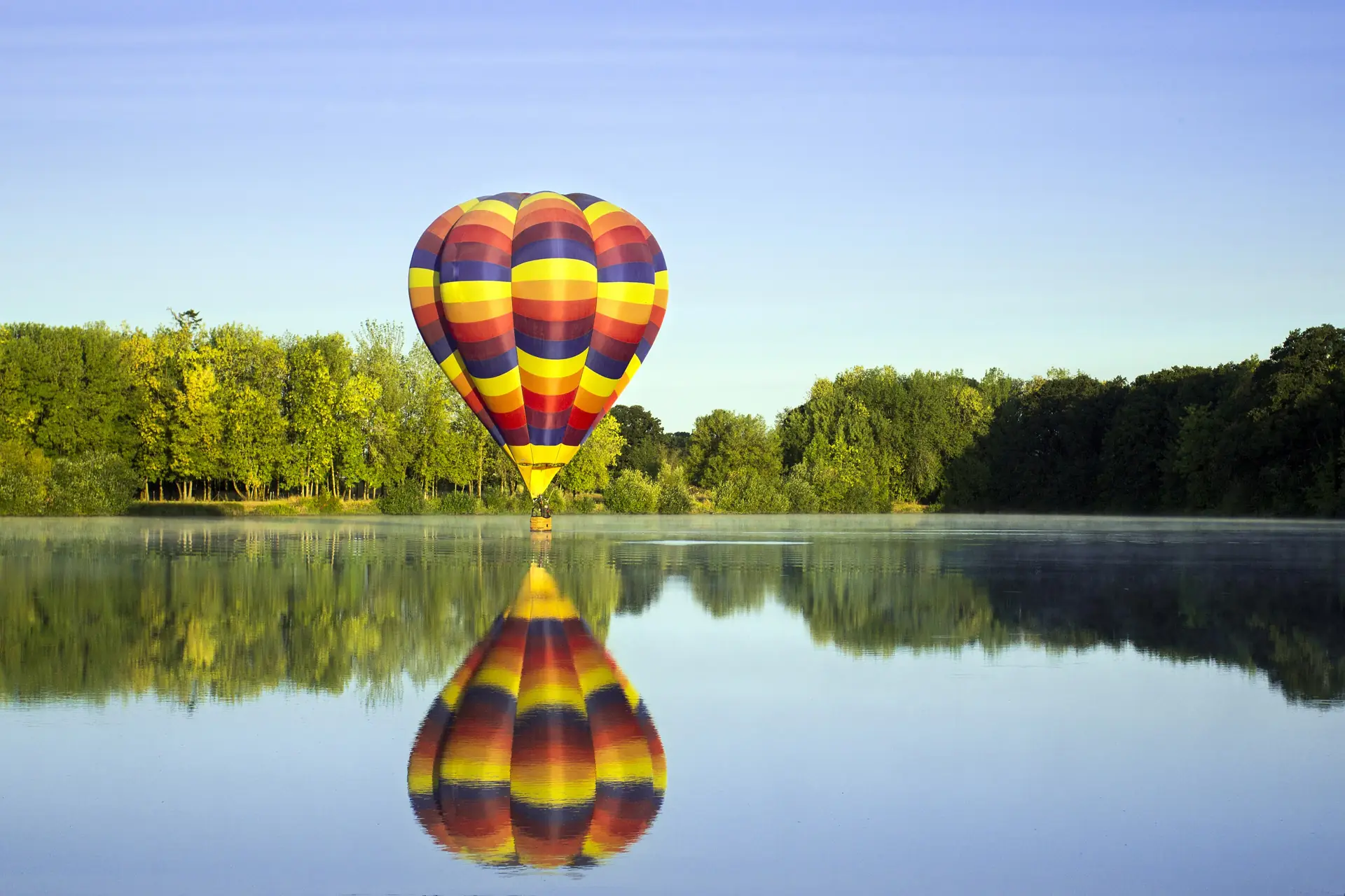 A hot-air balloon low over a still lake, reflected in the water