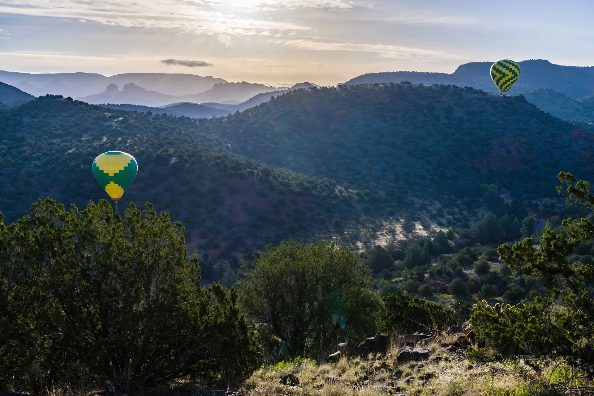 Heißluftballons treiben im Morgengrauen über die Wacholderflächen und roten Felsen des Angel Valley bei Sedona