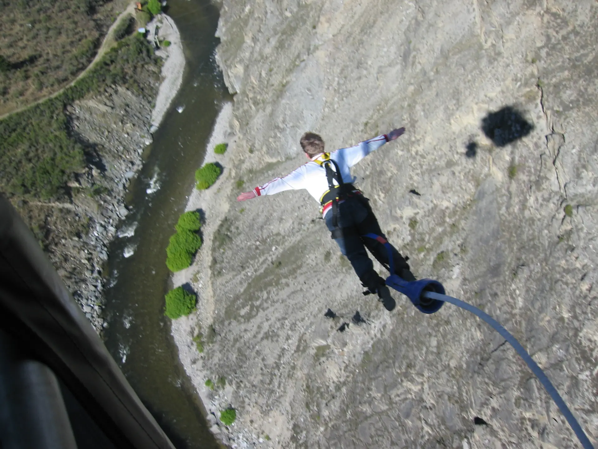A bungy jumper diving head-first from the Nevis pod, arms spread, with the dry Nevis gorge far below