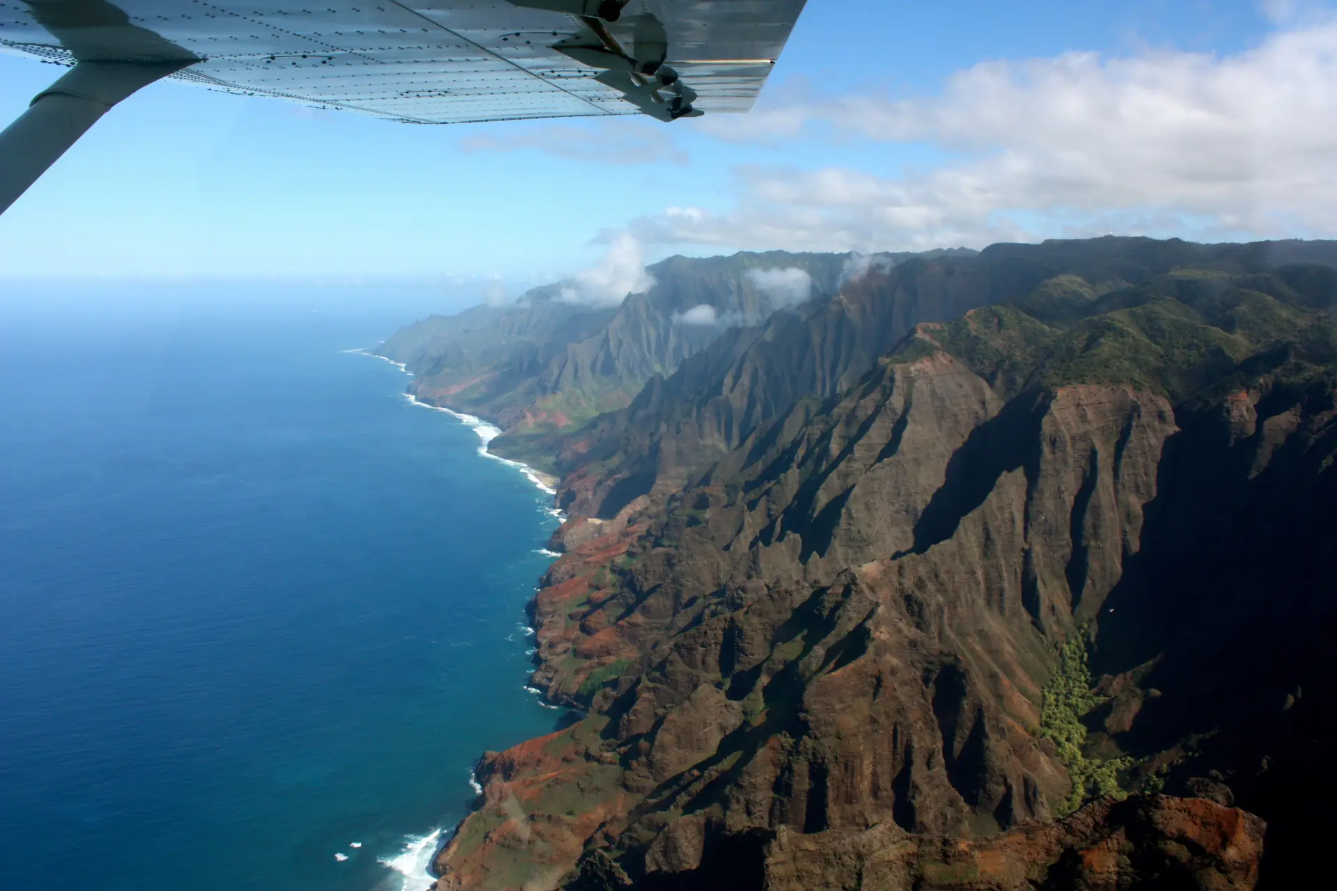 Die Nā-Pali-Klippen aus dem Helikopter, rote Grate und grüne Hänge über dem tiefblauen Meer