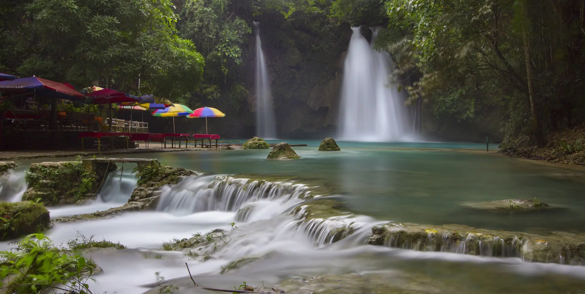 Kawasan Falls in Badian, Cebu: turquoise water pouring over a limestone ledge into a milky-blue pool under the jungle