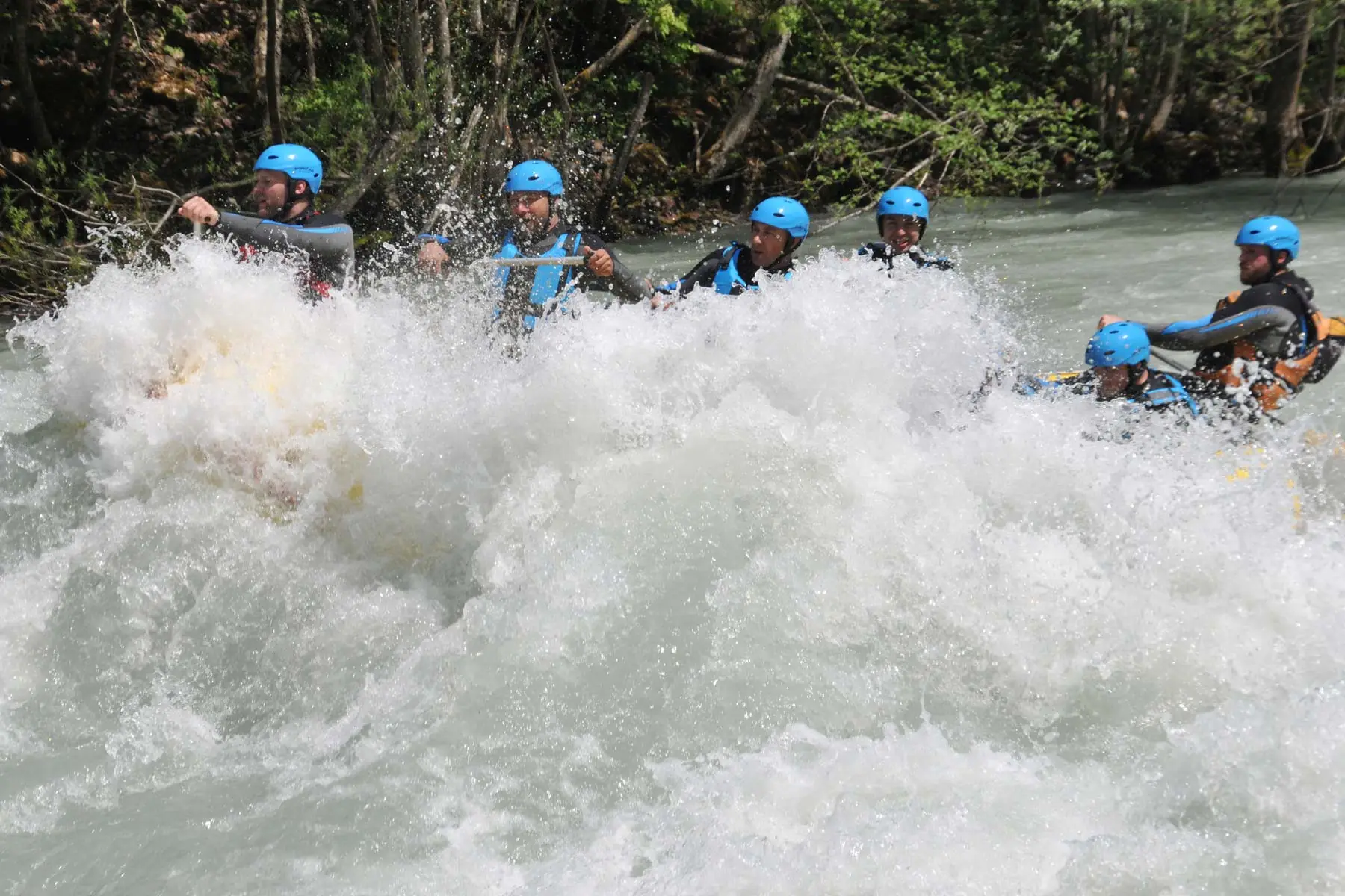 A raft of paddlers in blue helmets punching through a white rapid on the Tara