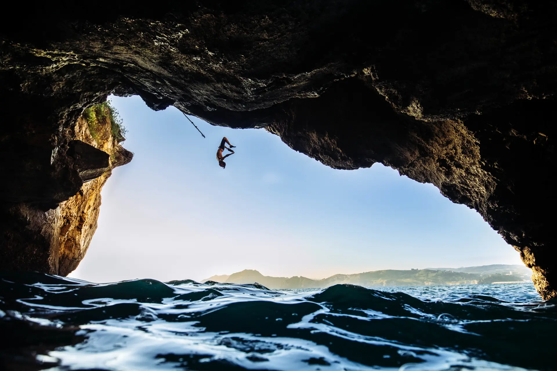 A climber letting go from the roof of a sea cave, falling towards the waves with the open sea beyond (symbolic image, not Mallorca)