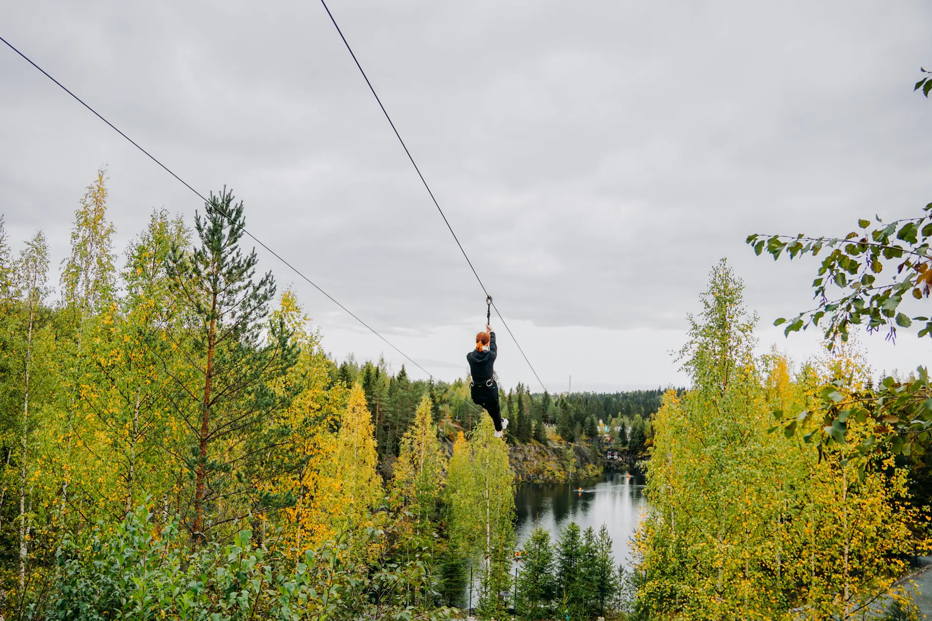A rider on a zipline trolley crossing high above a forest river (symbolic image, Karelia, not the Tara)