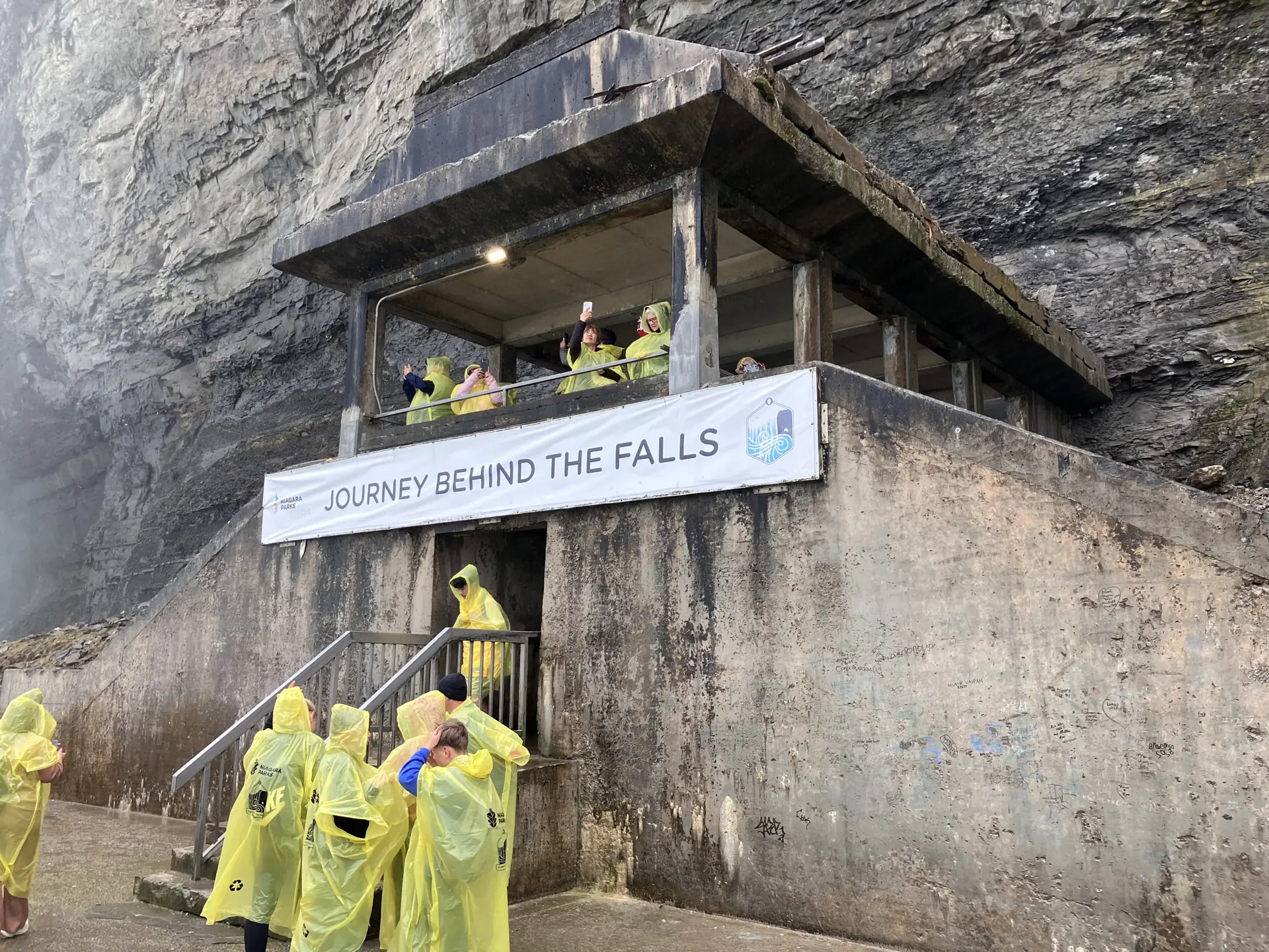 Besucher in gelben Ponchos auf dem unteren Aussichtsdeck von Journey Behind the Falls, daneben donnern die Horseshoe Falls