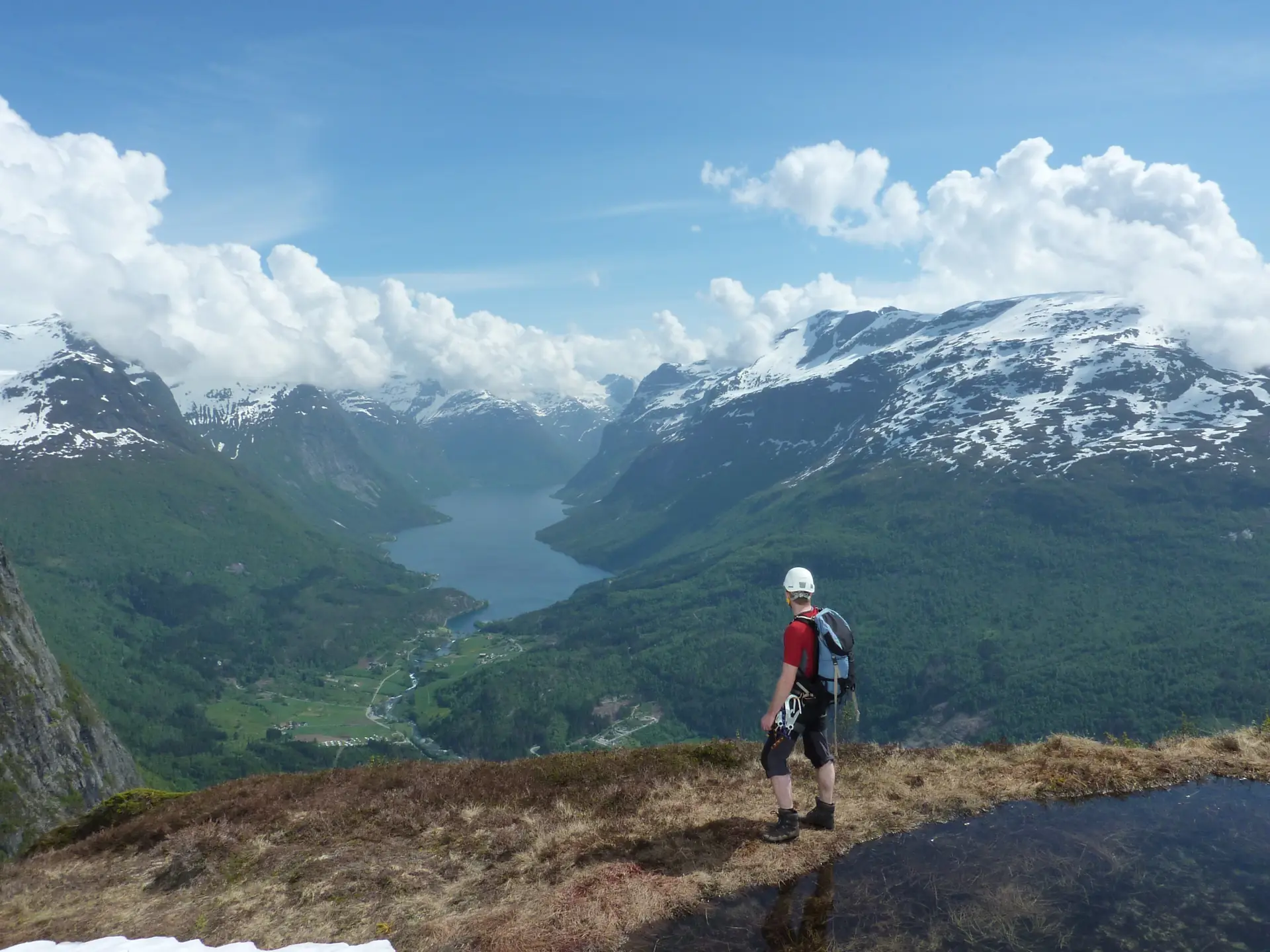 A climber in a helmet standing at the top of Via Ferrata Loen with the Nordfjord and snow-capped mountains spread out below