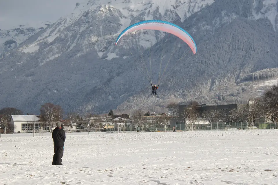 Tandem paragliders descending over the rooftops of Interlaken with the Bernese Alps behind