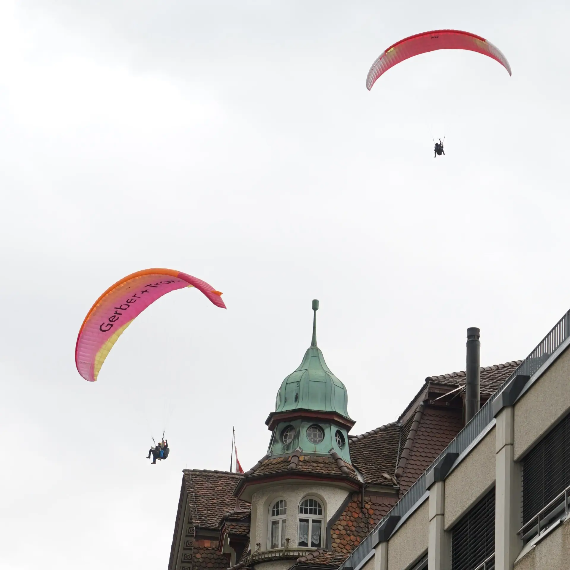 A tandem paraglider with a red and black wing high in a blue sky above Interlaken