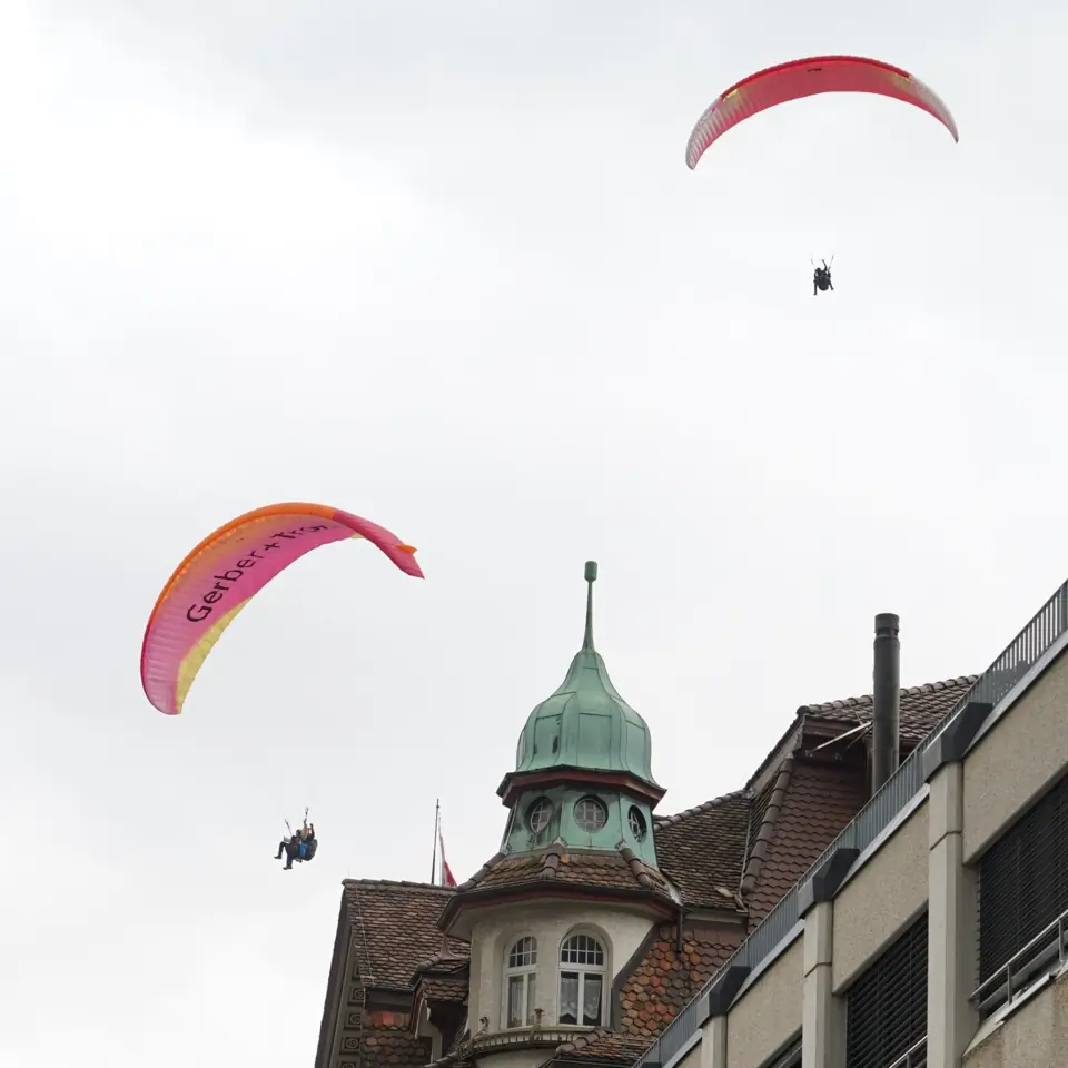 Ein Tandem-Gleitschirm mit rot-schwarzer Kappe hoch im blauen Himmel über Interlaken