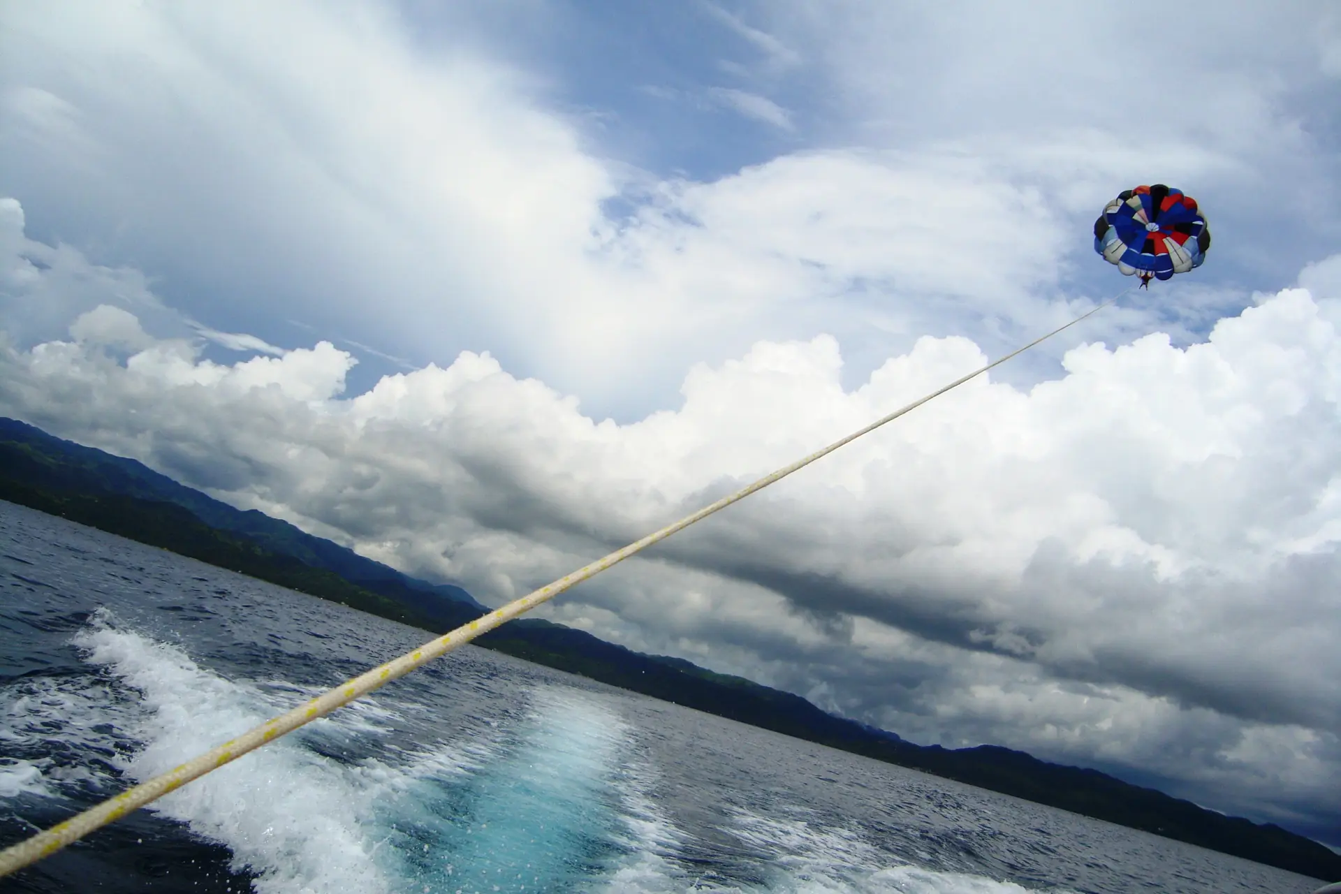 A parasail canopy high above the sea off Boracay, the tow rope running back to the boat's wake, hills of Panay behind