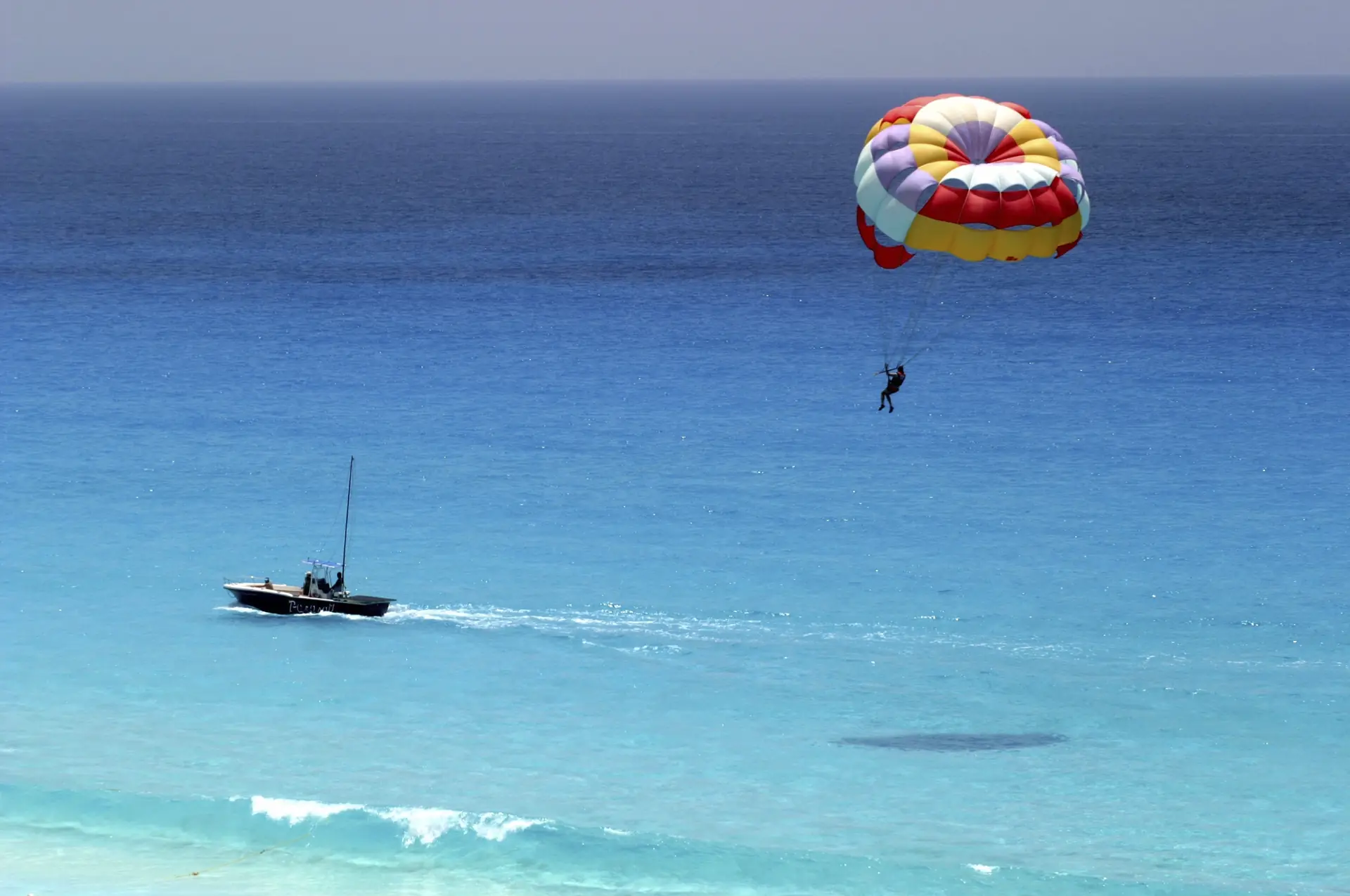 A parasailer under a red-and-yellow canopy towed by a boat over turquoise water off the Riviera Maya