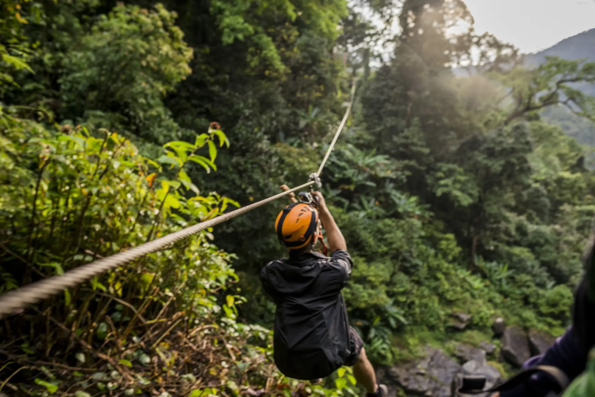 A rider in an orange helmet on a zipline over a jungle gorge, seen from behind (symbolic image, Laos, not Loboc)