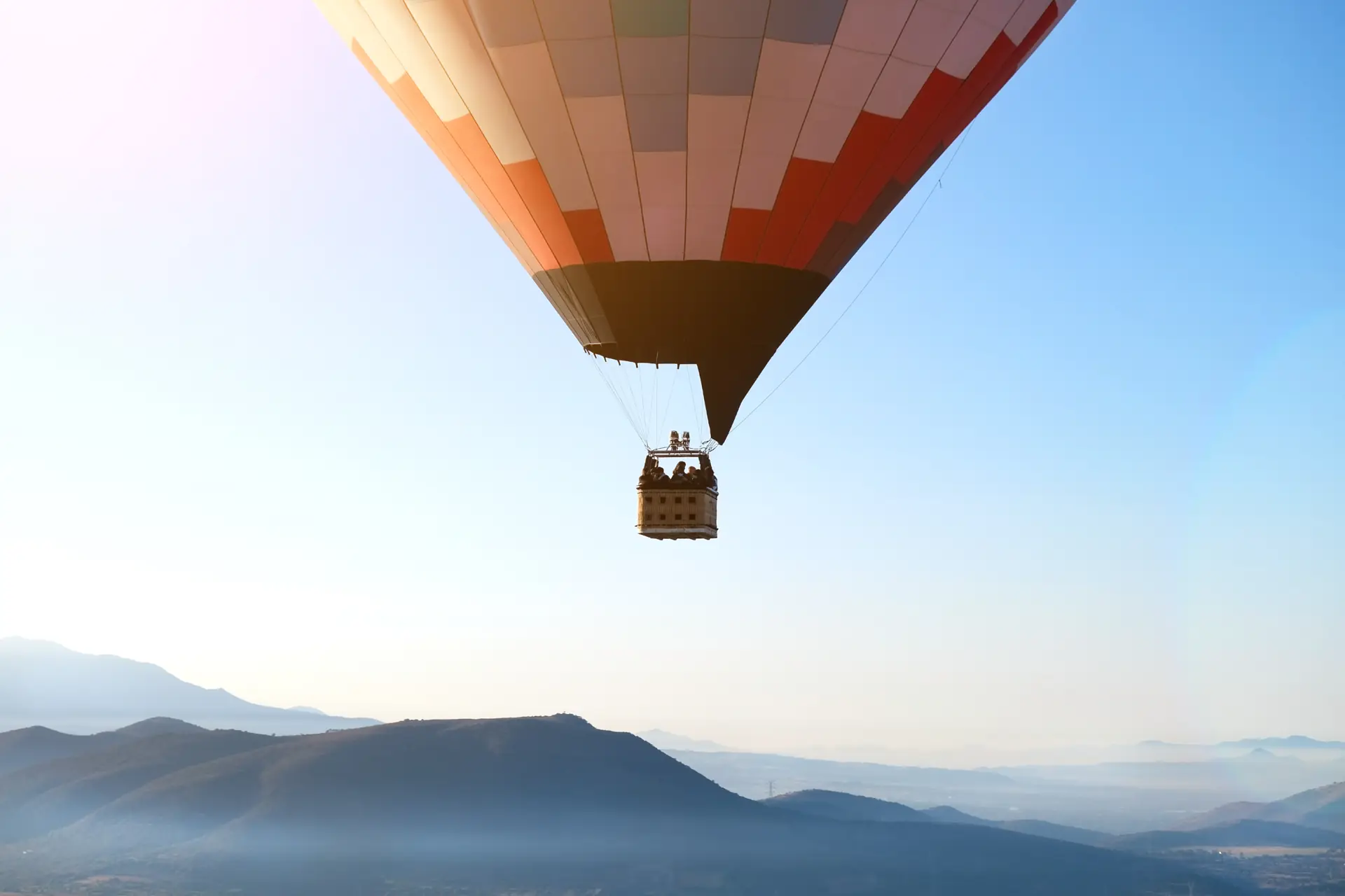 A striped hot-air balloon with passengers floats over hazy desert mountains (symbolic image, not north Phoenix)