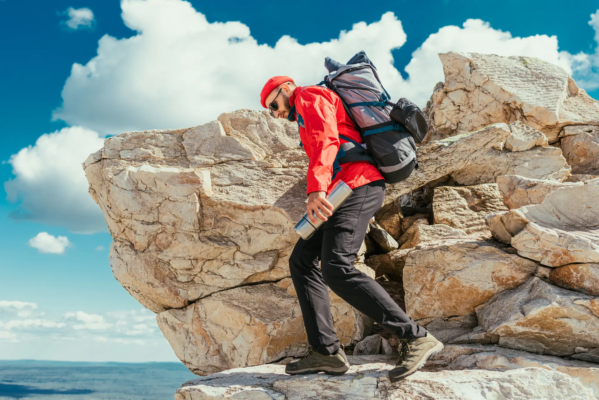 A hiker in a red jacket scrambles hand over hand up a red rock face (symbolic image, not Camelback)
