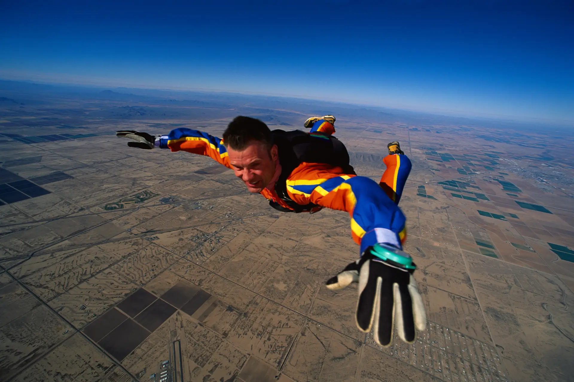 A skydiver in freefall in a blue suit high over flat brown desert farmland (symbolic image, not Eloy)