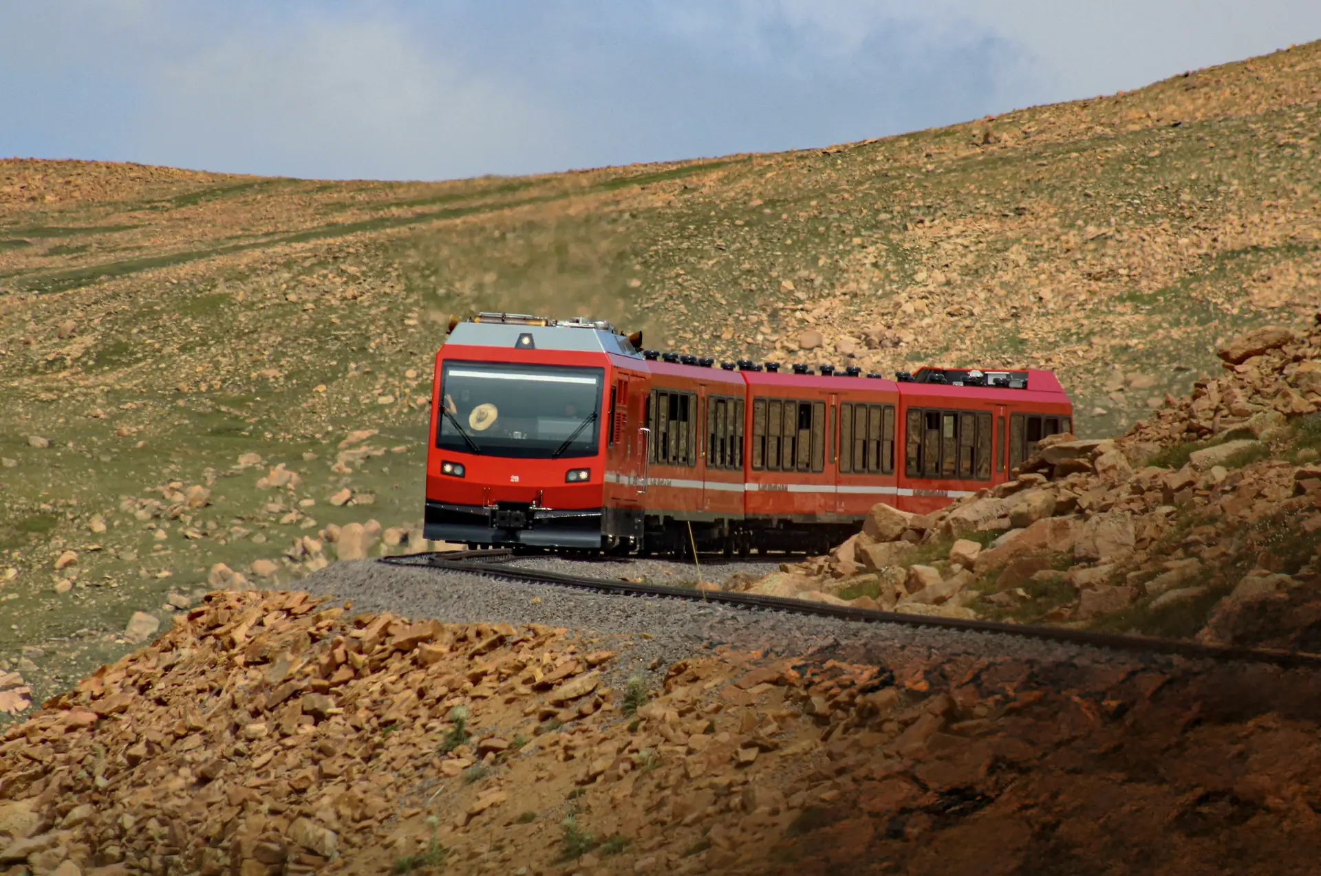 Ein roter Zug der Pikes-Peak-Zahnradbahn klettert über die felsige Tundra nahe dem Gipfel