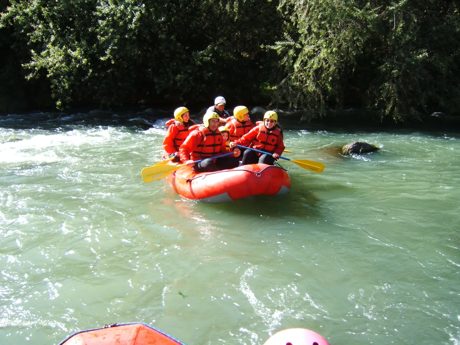 Ein rotes Raft mit fünf Paddlern in Helm und Weste schlägt durch eine Wildwasserwelle auf einem grünen Andenfluss (Río Chili, Arequipa, nicht der Urubamba)