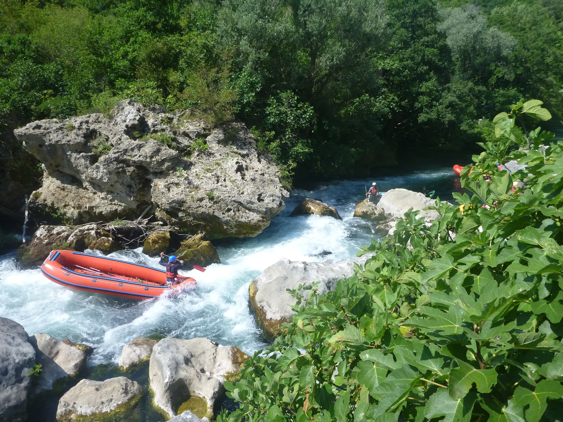 Ein rotes Raft mit Paddlern fädelt sich zwischen Felsblöcken durch eine Stromschnelle der grünen Cetina
