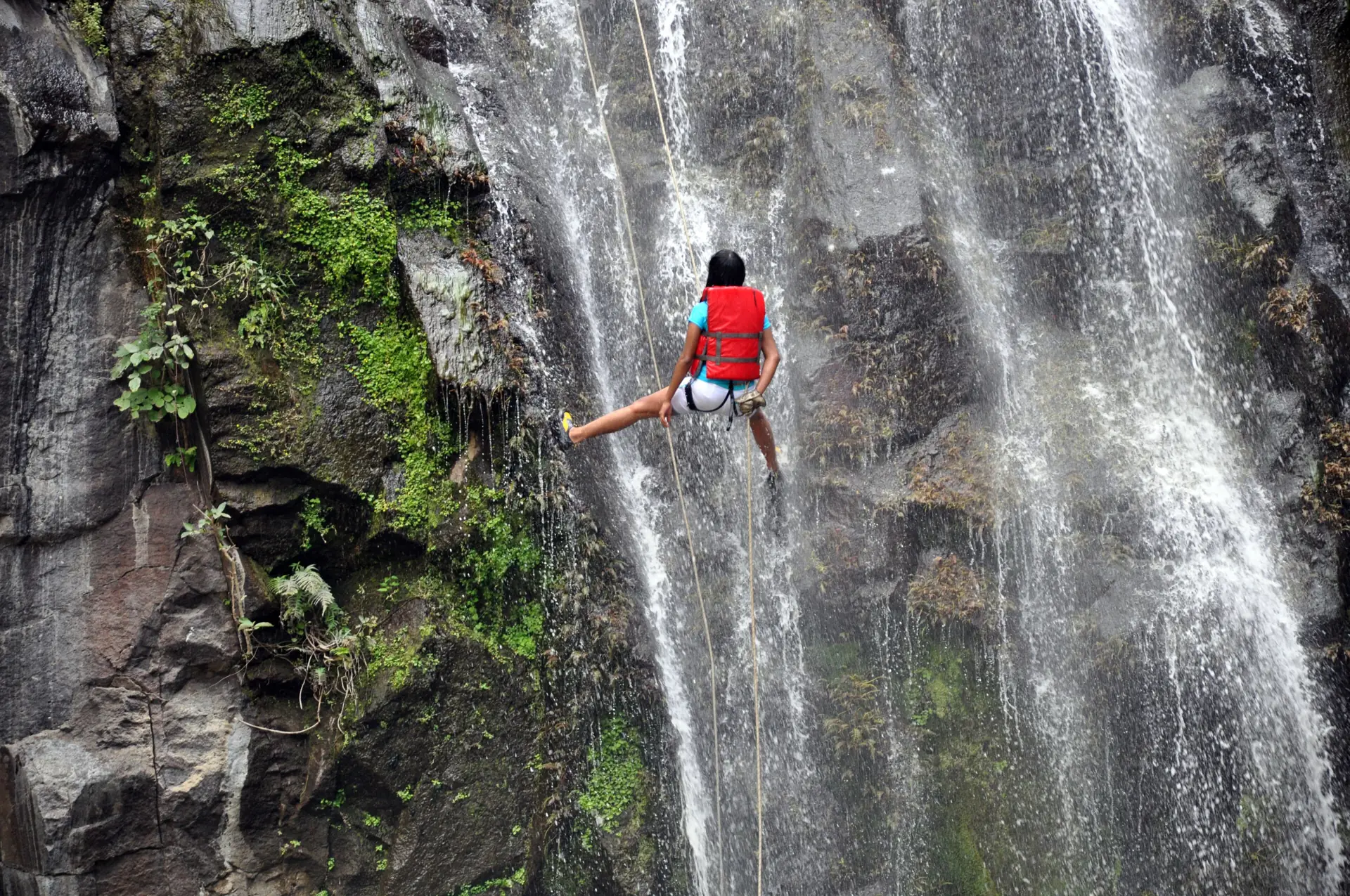 Ein Canyoner seilt sich an einem Wasserfall in einer grünen Schlucht ab