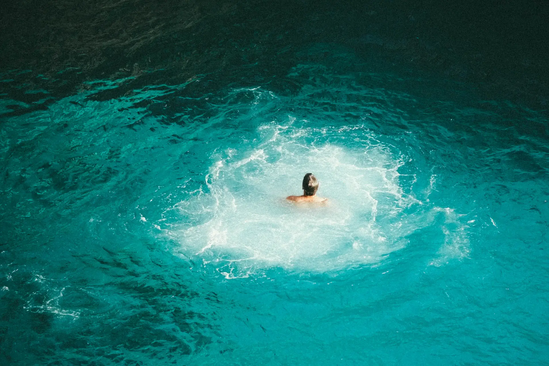 A swimmer surfacing in the clear turquoise water at the foot of the cliffs below Rick's Café