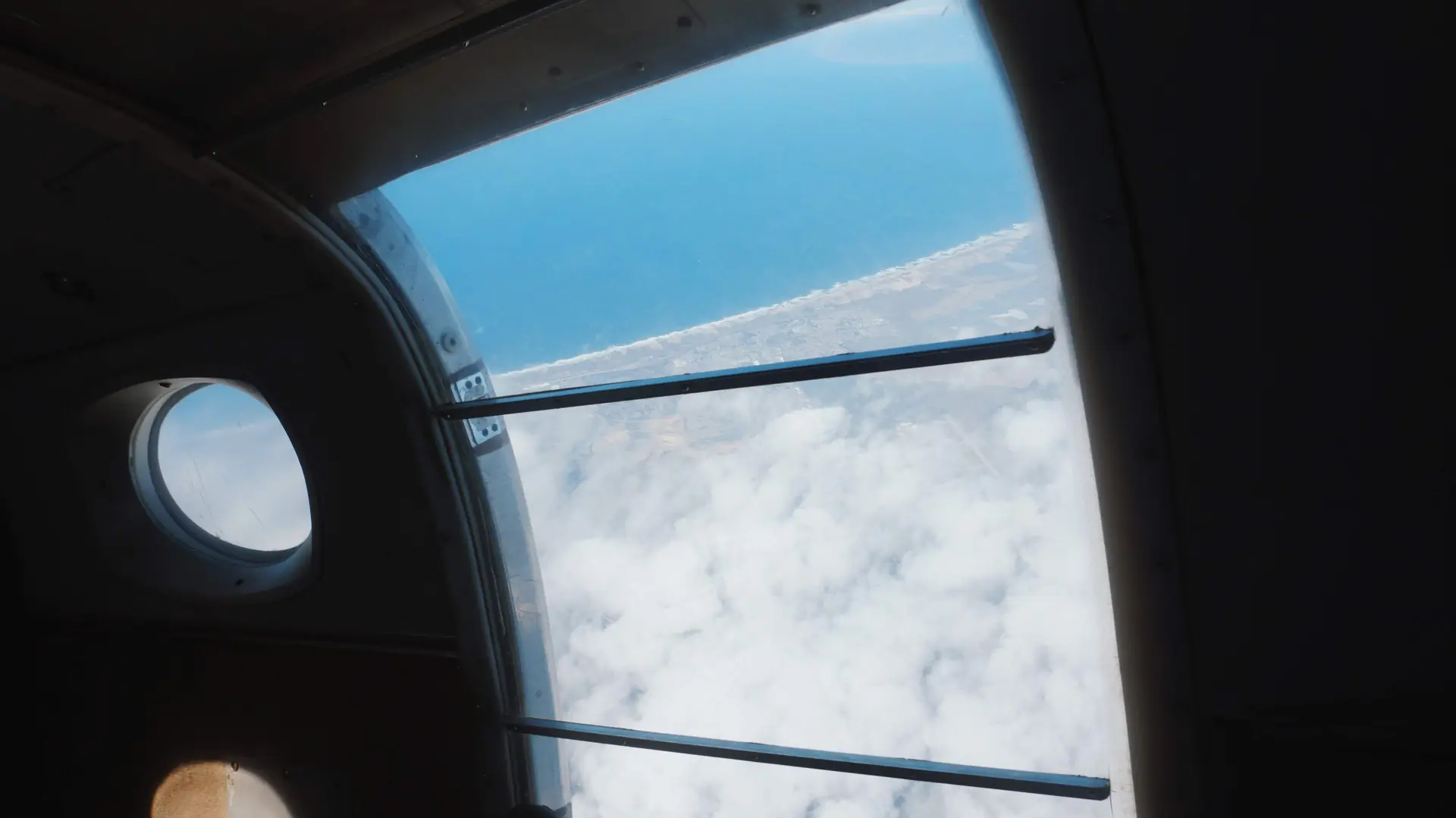 The open door of a skydiving plane with a layer of cloud and the ground far below (symbolic image, not Voss)