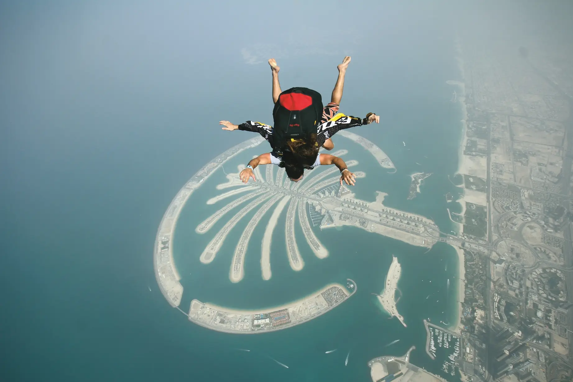 A tandem skydiver under canopy above Palm Jumeirah and the Gulf