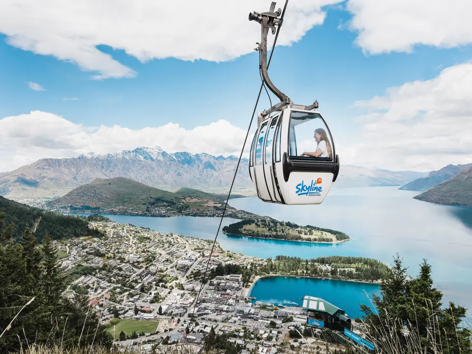 A Skyline gondola cabin rising above Queenstown with Lake Wakatipu, the peninsula and the Remarkables behind