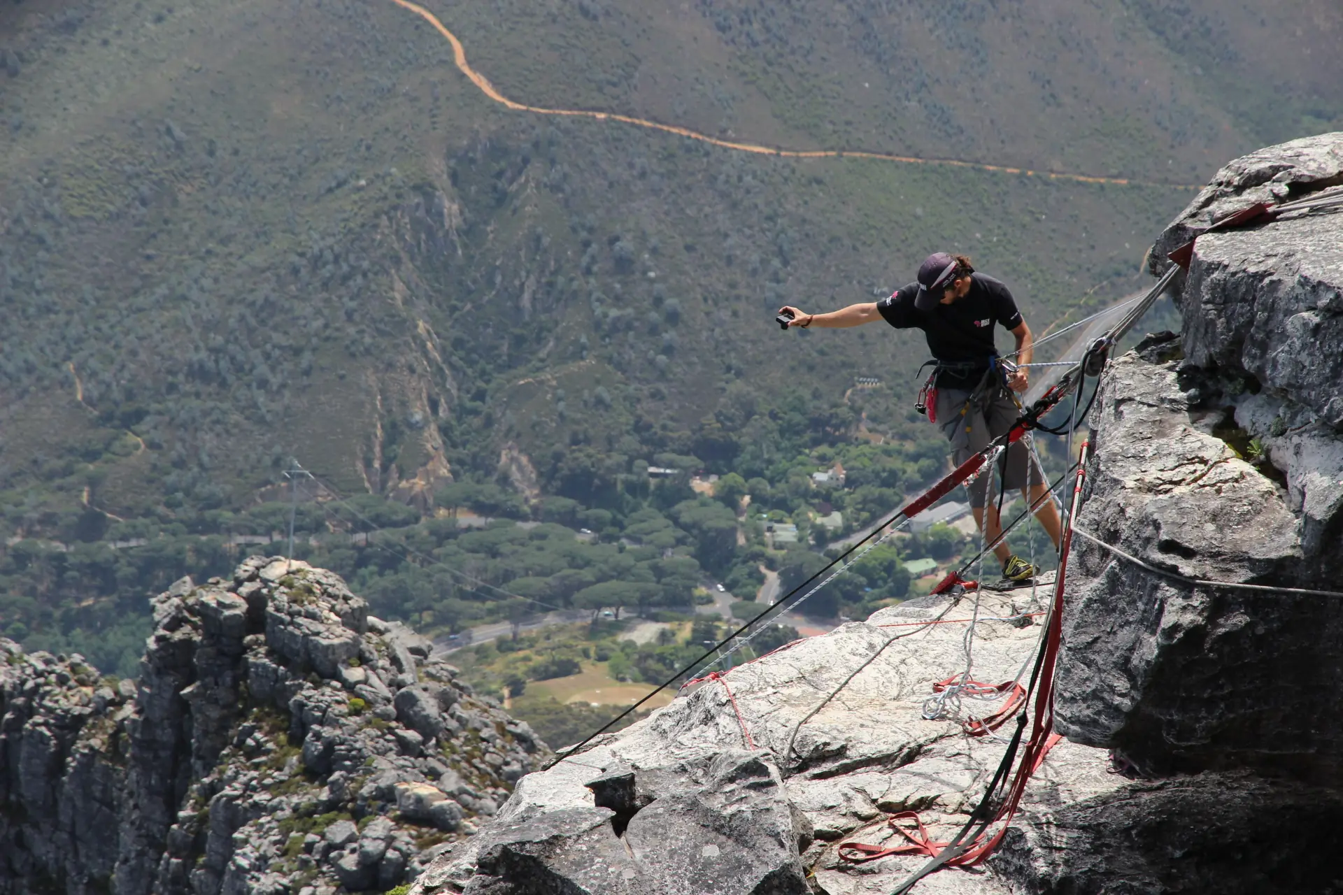 An abseiler leaning back over the edge of Table Mountain on a rope with Camps Bay and the Atlantic far below