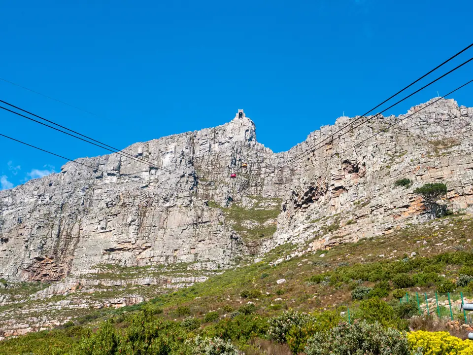 A red rotating cable car of the Table Mountain Aerial Cableway climbing above Cape Town with Lion's Head and the Atlantic behind
