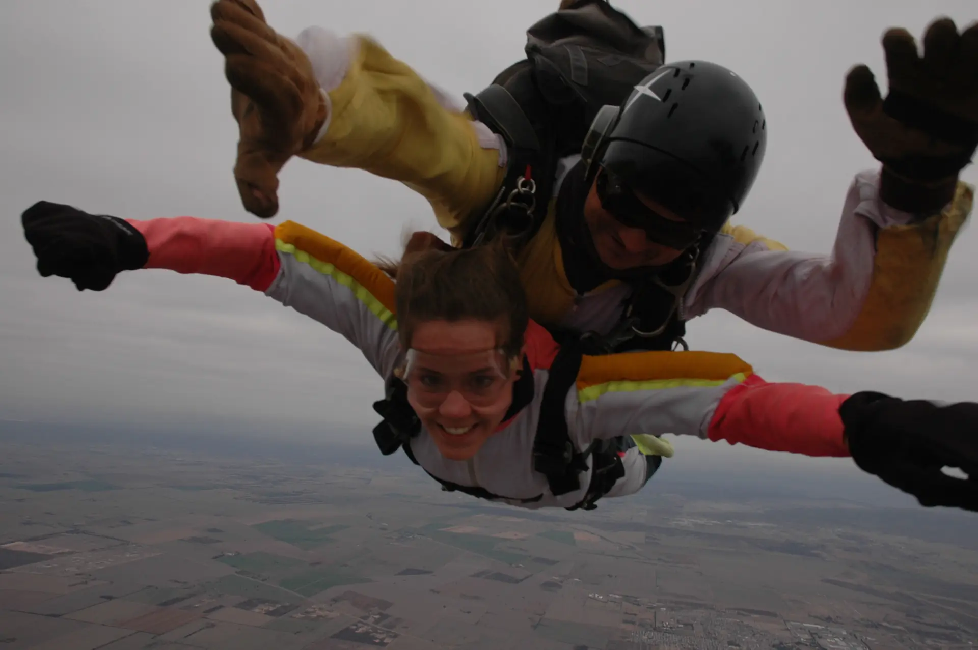 A tandem skydiving pair in freefall, the passenger grinning at the camera (symbolic image, not Interlaken)