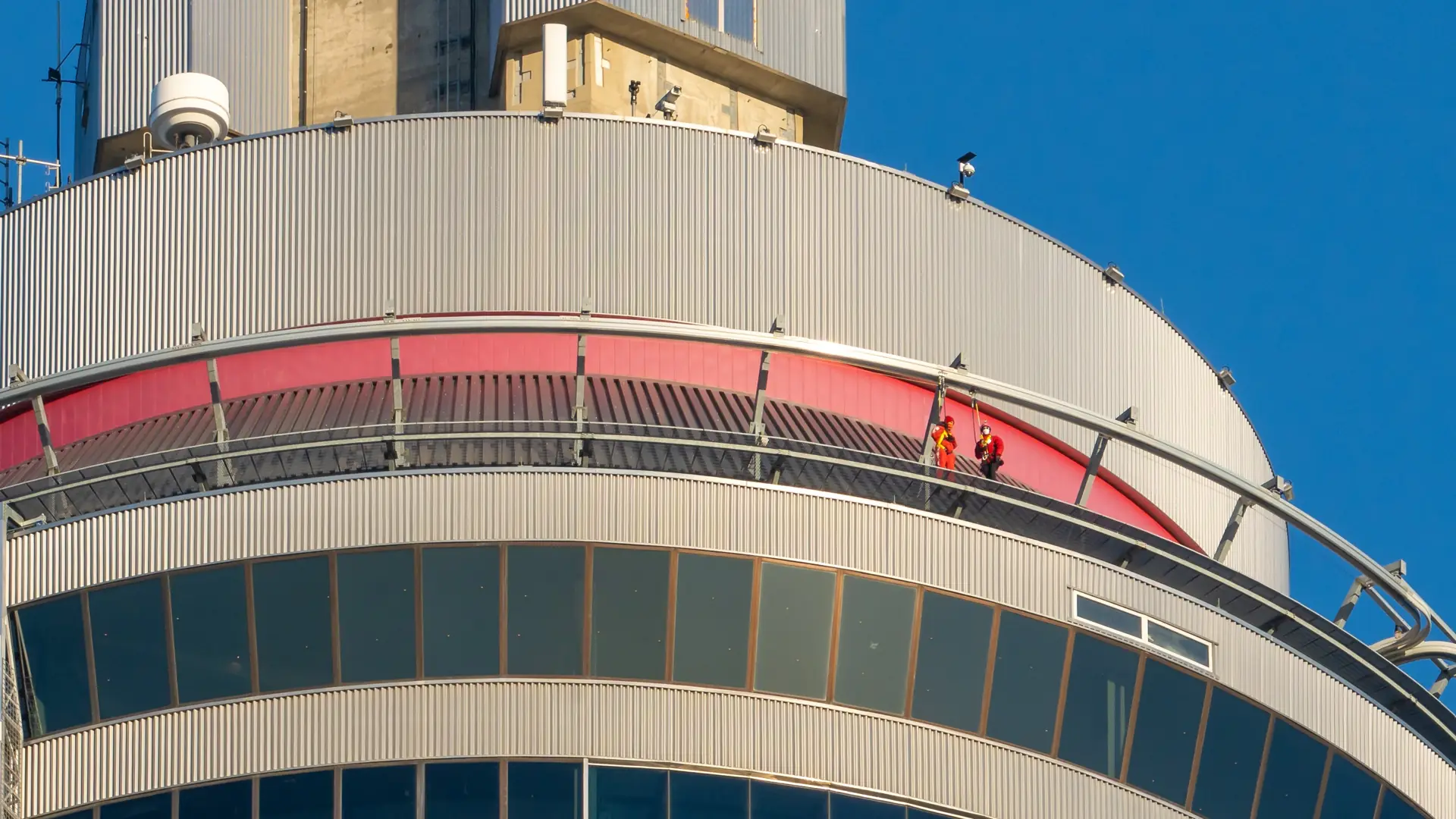 Zwei EdgeWalker in roten Anzügen auf dem schmalen Sims um die Spitze der Hauptkanzel des CN Tower