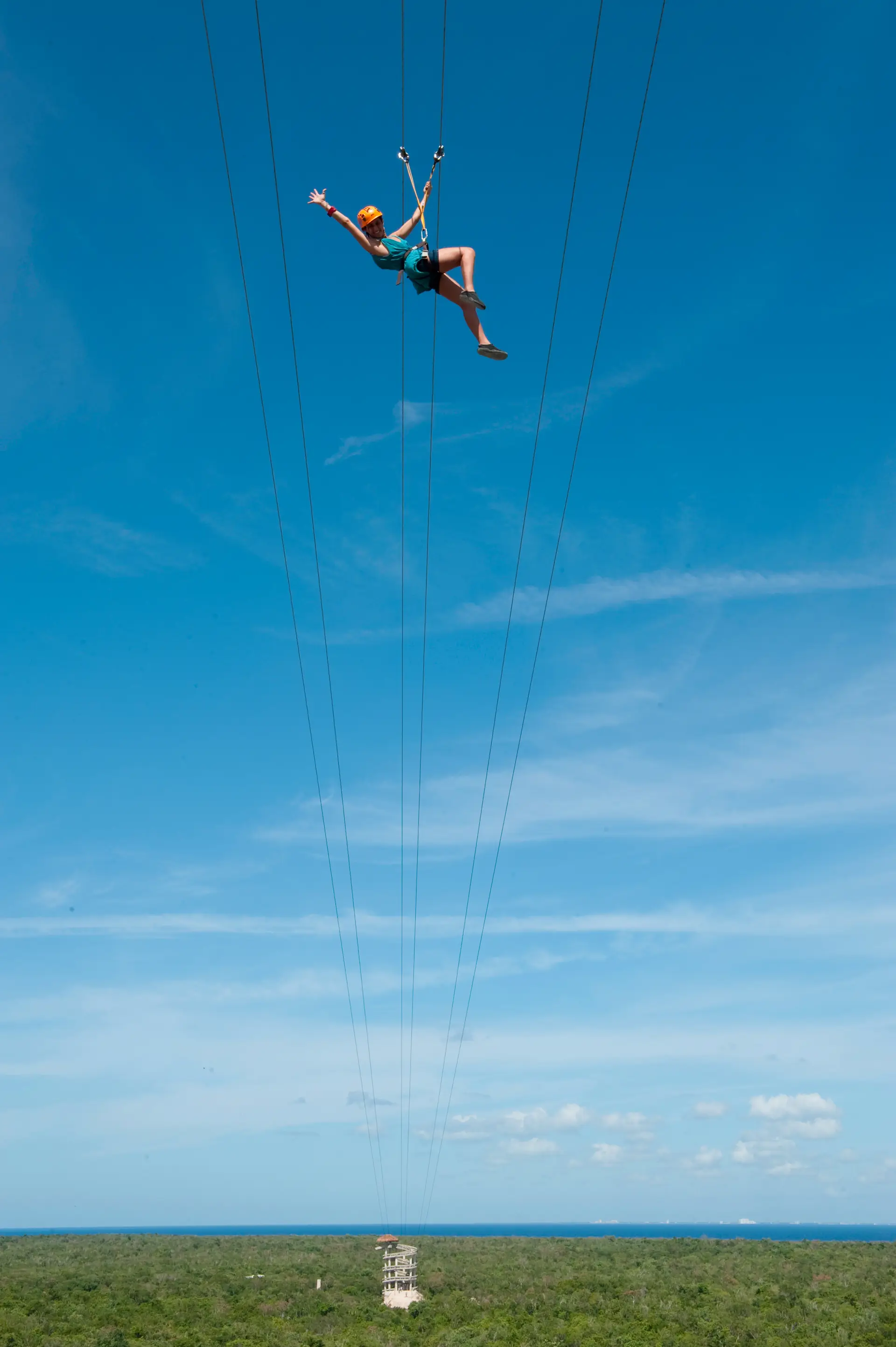 A rider on one of Xplor's ziplines high above the jungle, arms out, the Caribbean on the horizon