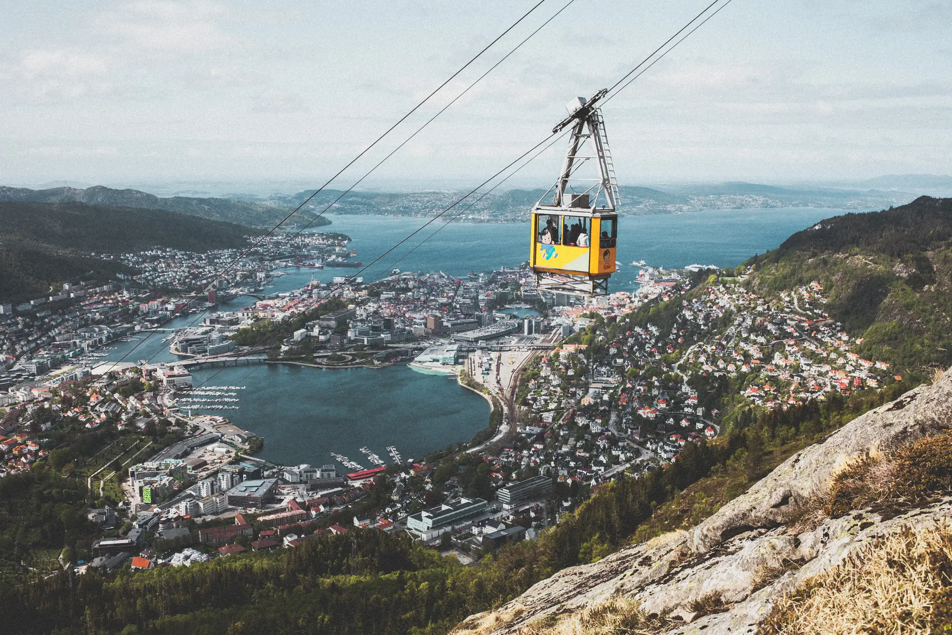 A yellow Ulriken cable car rising above Bergen with the city, the harbour and the islands spread out below