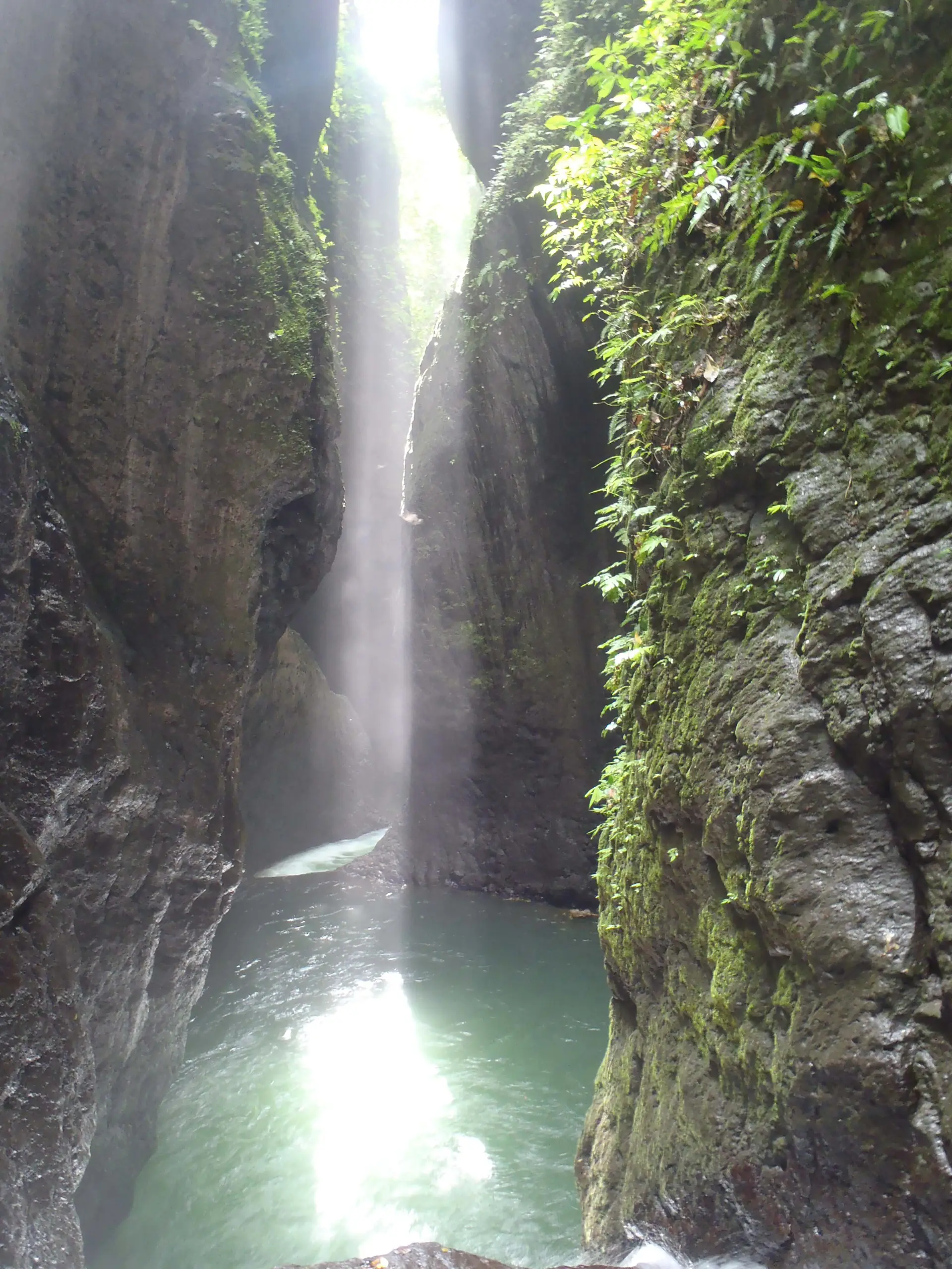 A narrow volcanic rock gorge with a waterfall dropping into a green pool in northern Bali