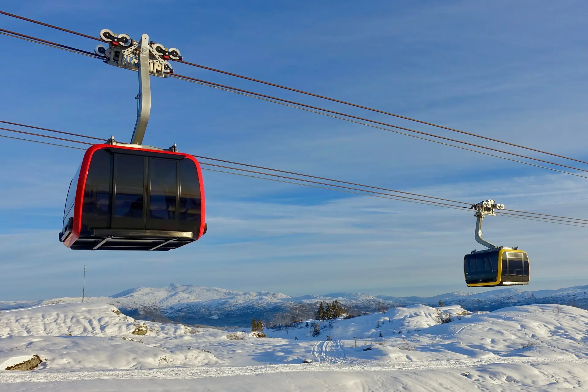 Two Voss Gondol cabins arriving at the Hangurstoppen top station in snow, with the mountains around Voss behind