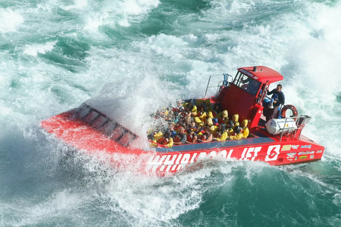 Das rote Whirlpool-Jetboot voller Passagiere pflügt durch das Wildwasser der Devil's-Hole-Stromschnellen