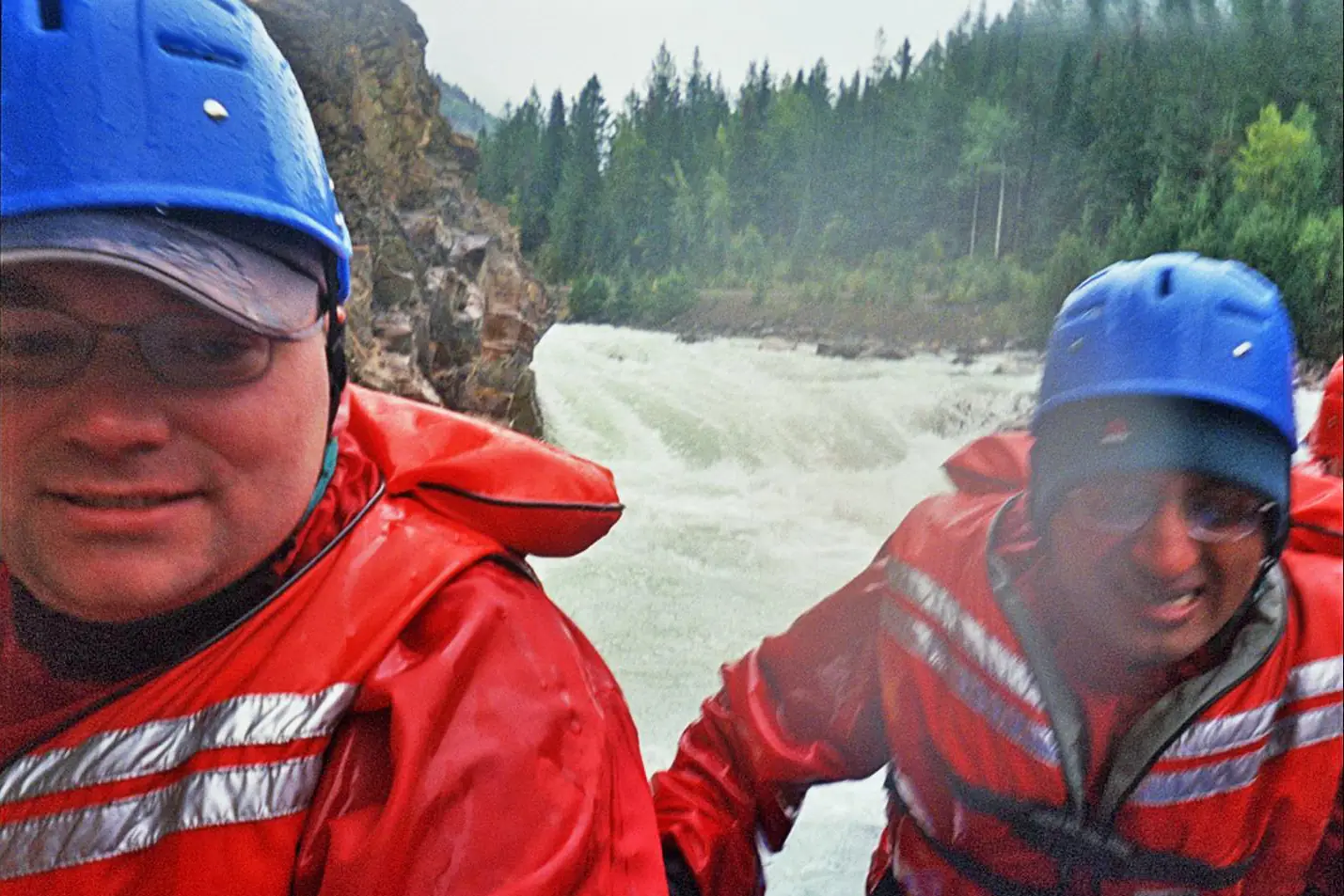 Two rafters in red jackets and helmets in front of the churning class 4 whitewater of the Kicking Horse River